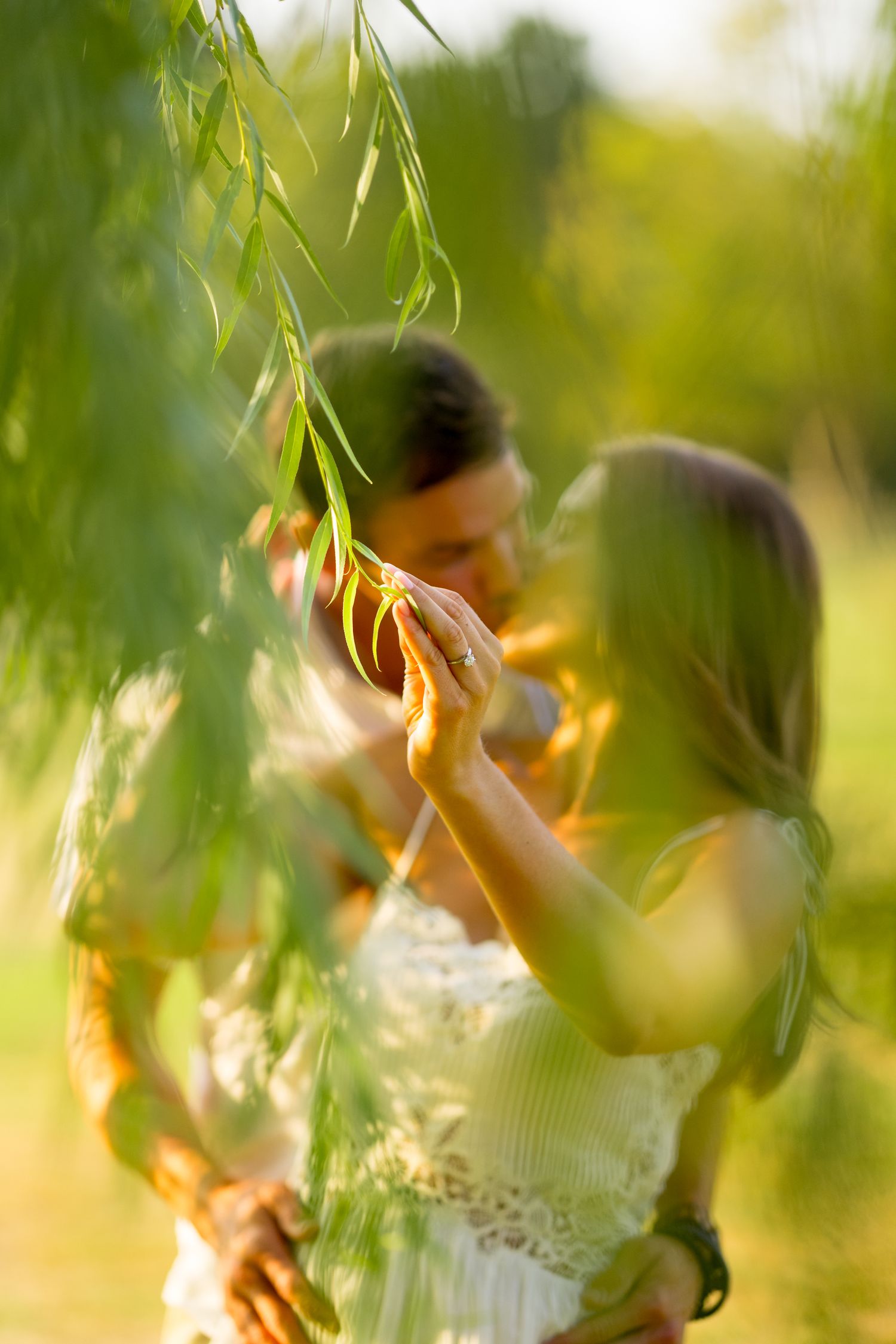 Romantic dance sequence captured through willow tree branches in soft natural lighting.