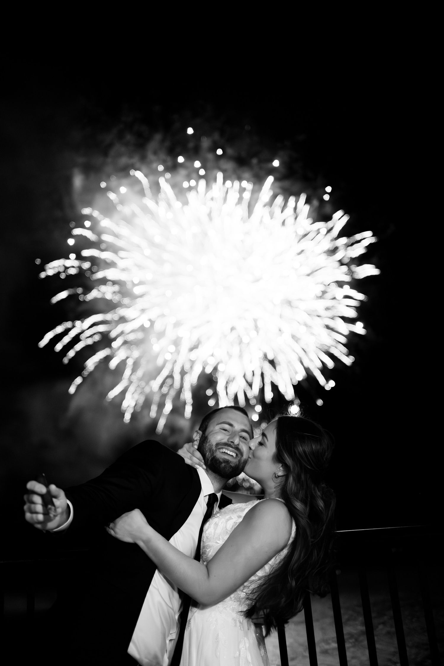 Black and white photo of fireworks display creating dramatic light streaks in night sky.