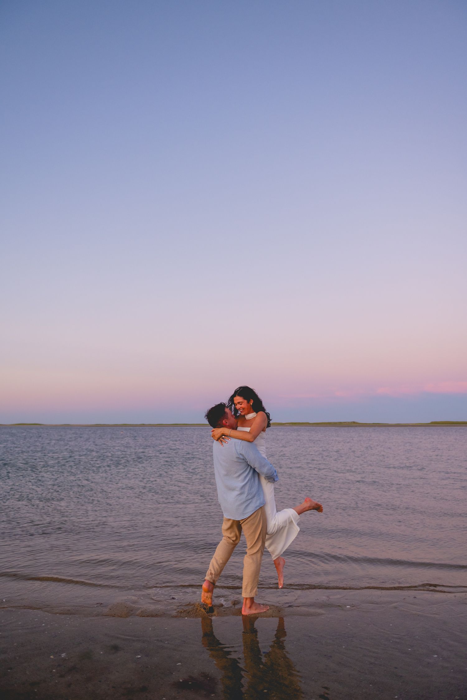 Romantic couple dancing on Cape Cod beach at sunset with ocean waves in background.
