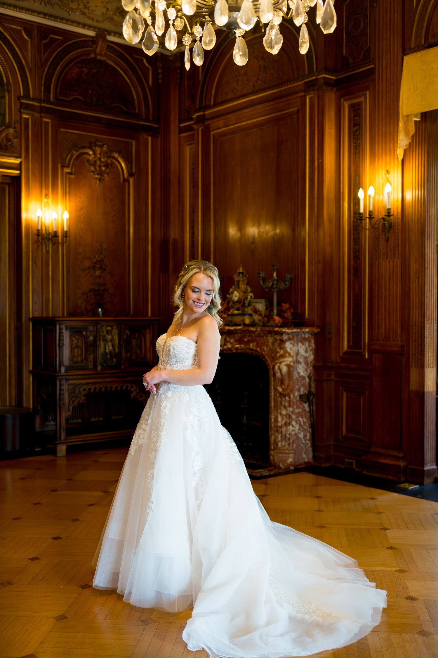 A bride in a flowing white wedding gown twirls gracefully in an elegant ballroom with crystal chandeliers and ornate decor.