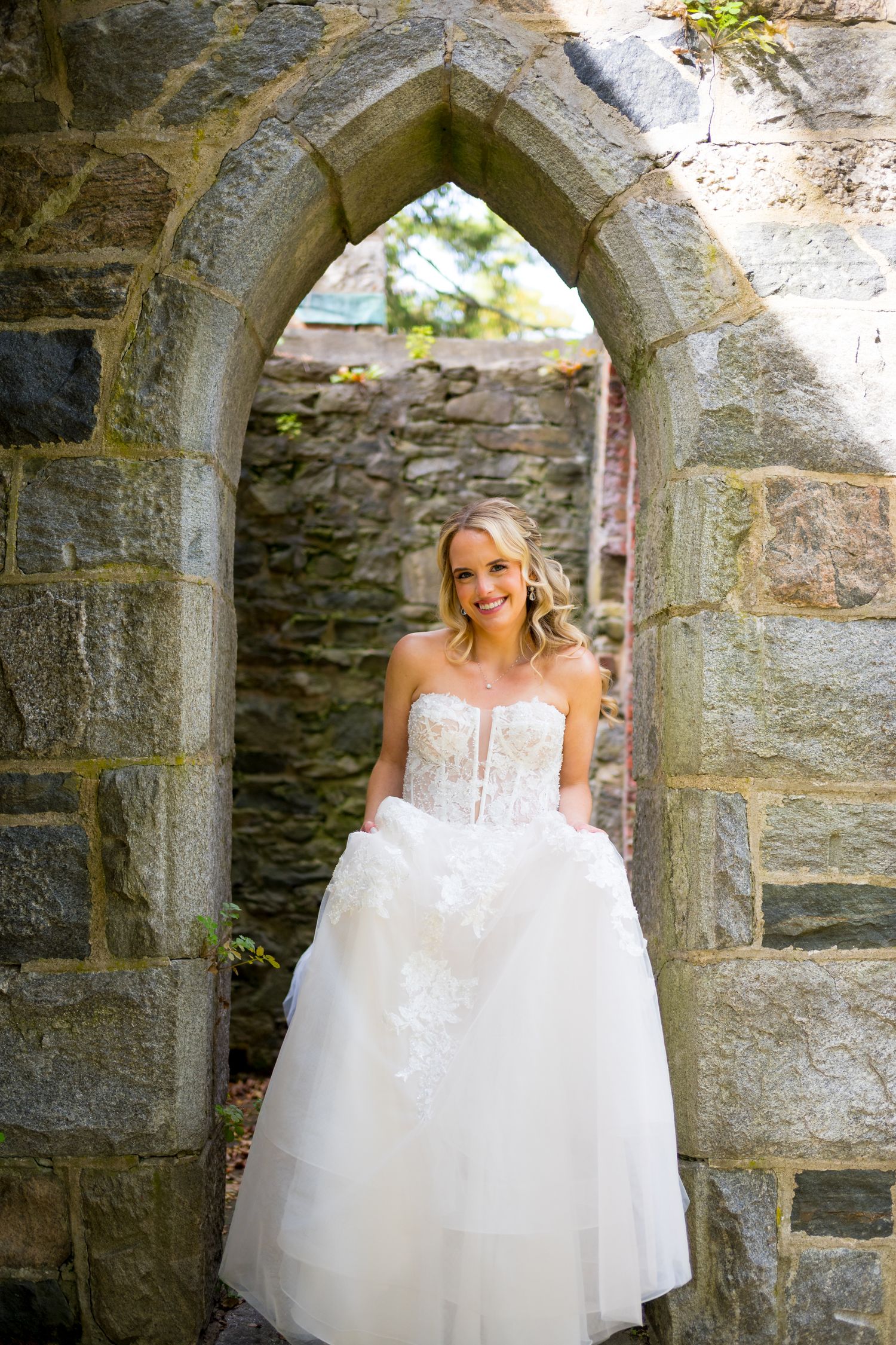 A stunning white wedding dress with a strapless bodice and tulle skirt framed by a stone archway.