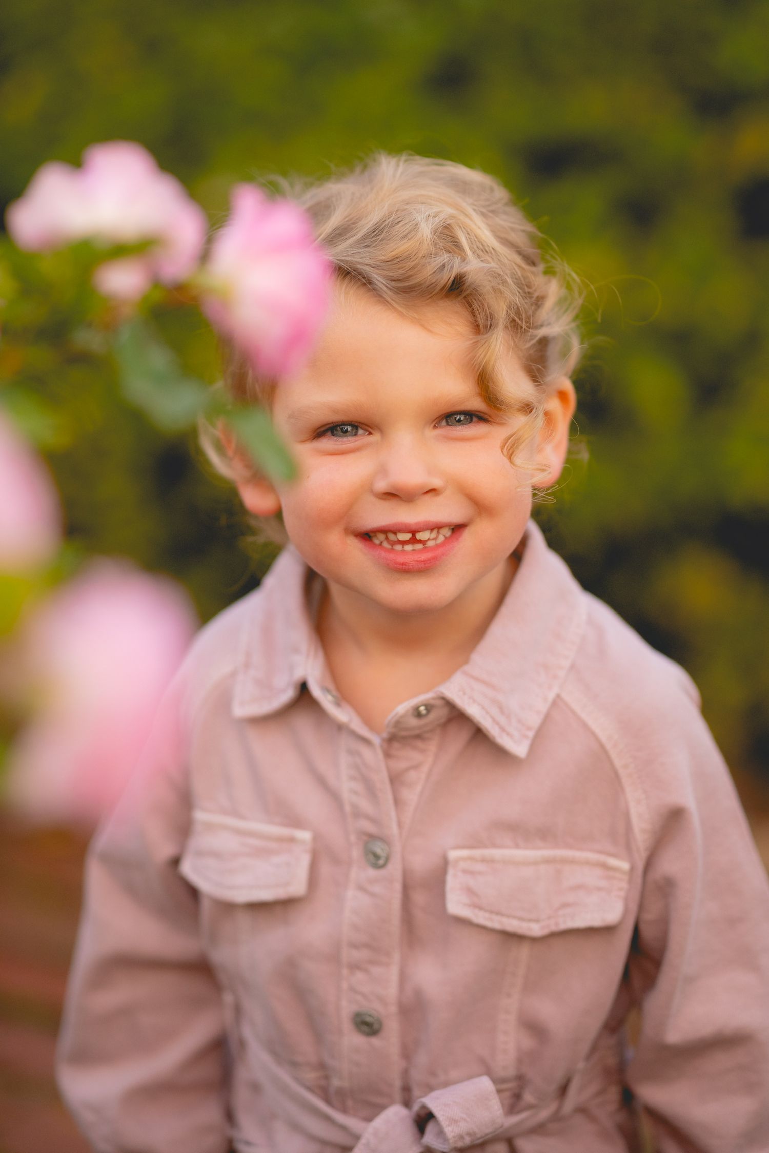Child in pink jacket smiling outdoors with soft focus background.