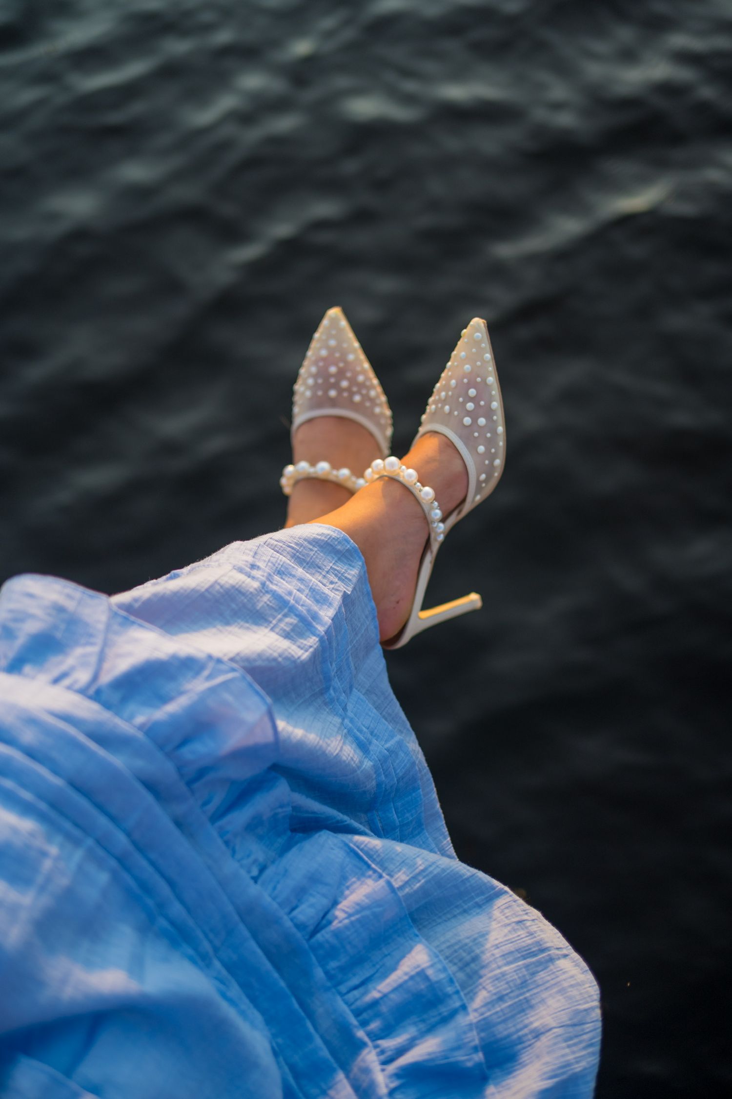 Sparkly high heel shoes against dark water background in blue light.