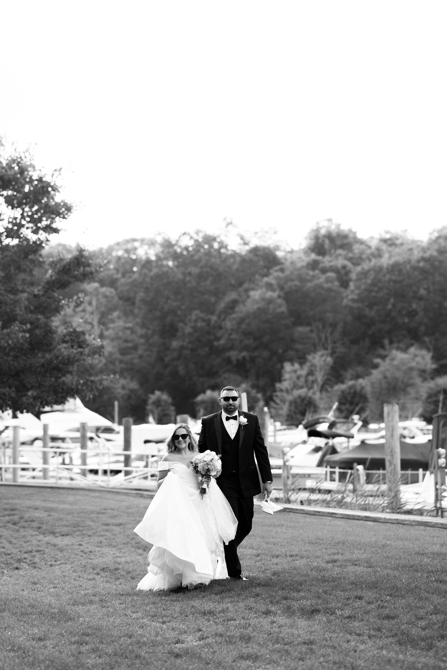 Black and white photo series of couple walking across grassy field with boats in background.