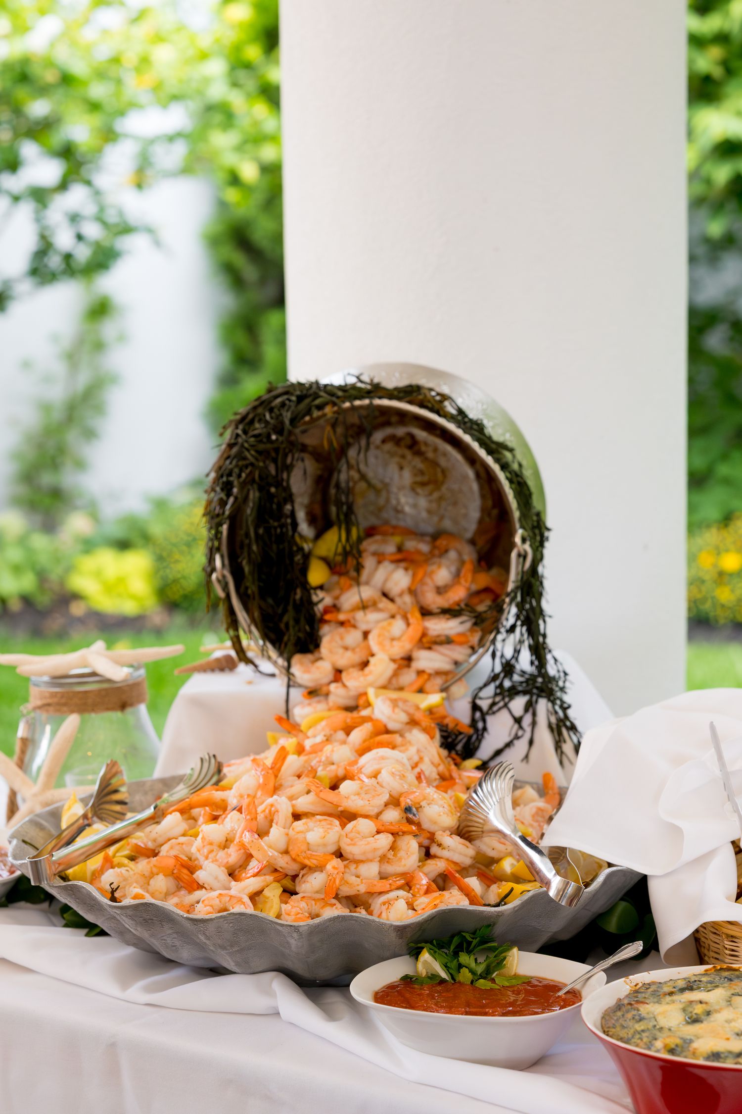 Large display of chilled shrimp cocktail with dipping sauces at an elegant outdoor catered event.