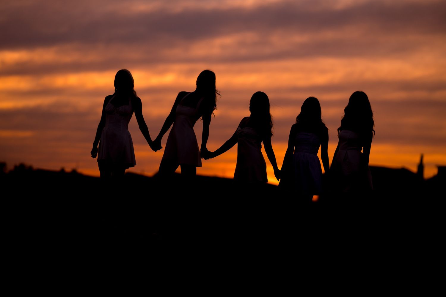 Silhouettes of Fairfield University graduates standing together against a dramatic orange sunset sky for graduation photos.