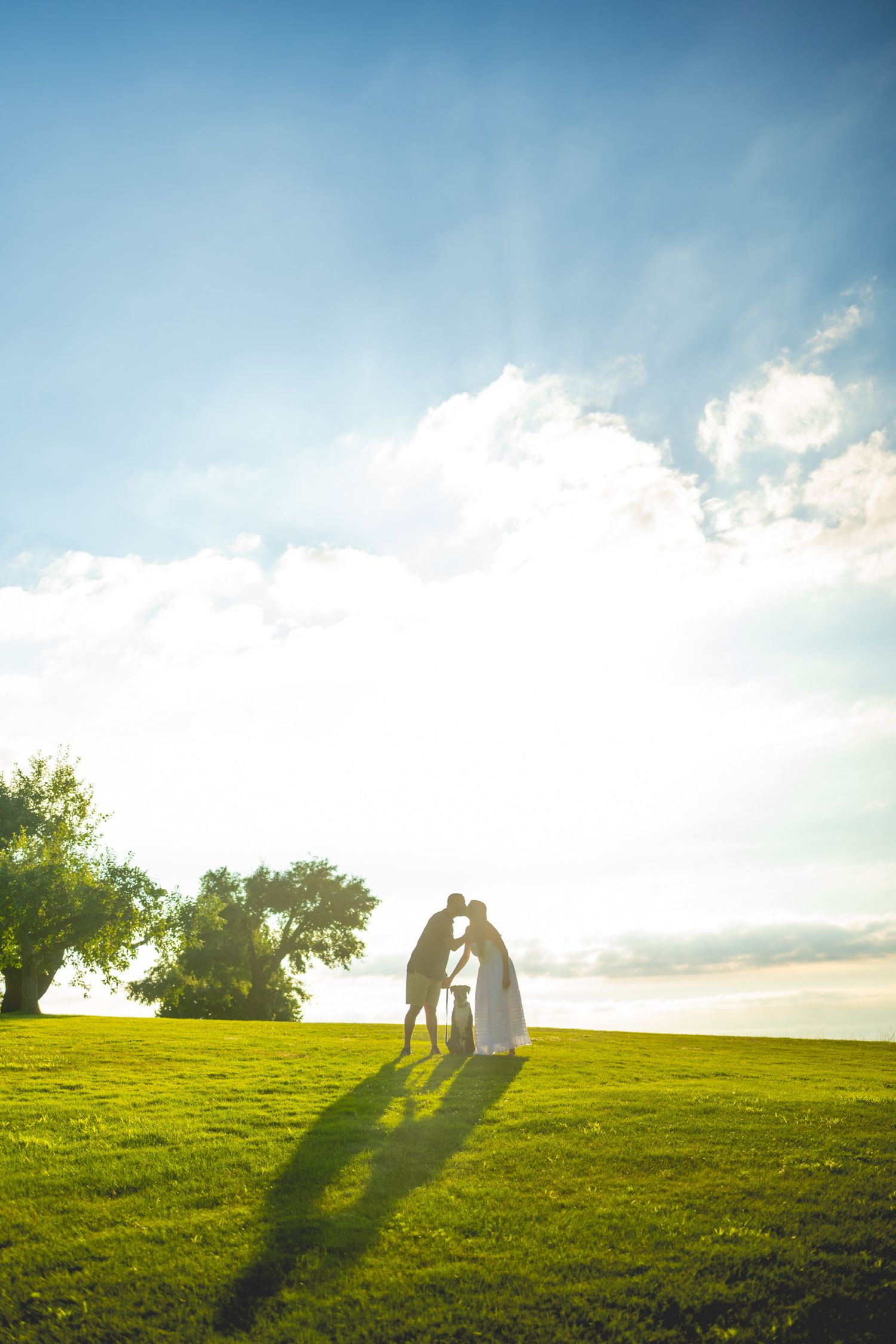 Silhouetted couple standing on hilltop against bright sunset sky.