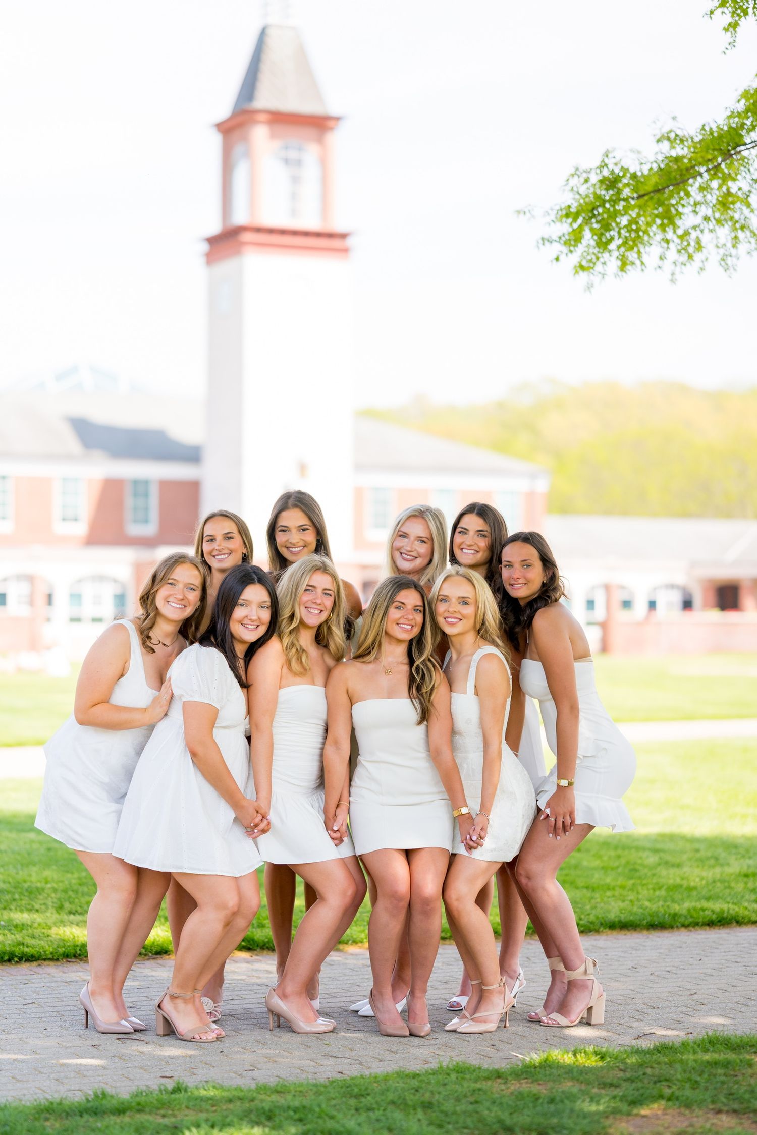 Quinnipiac University graduates poses in white dresses on grass with church building in background.