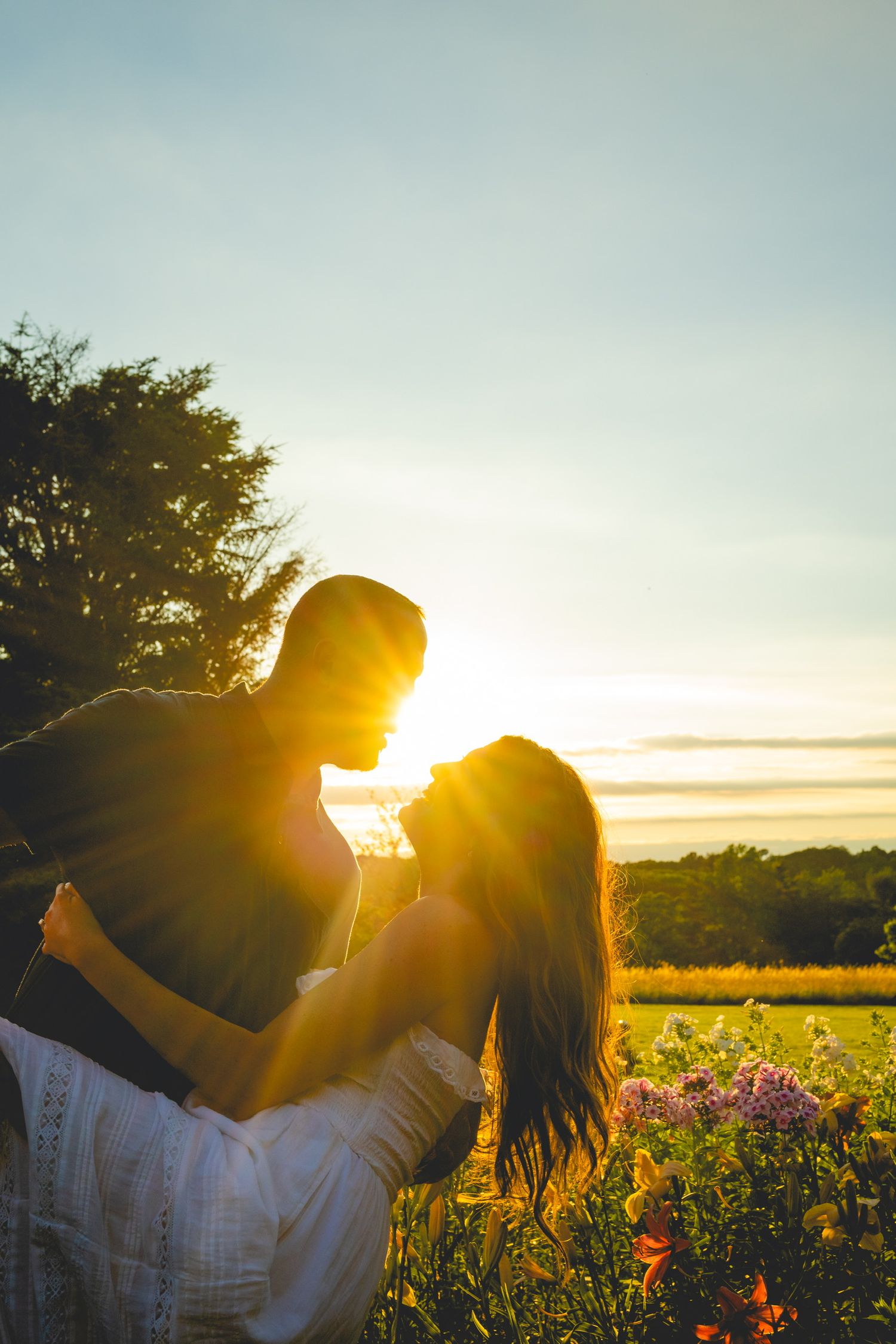 Silhouetted couple embracing in flower field during dramatic sunset.