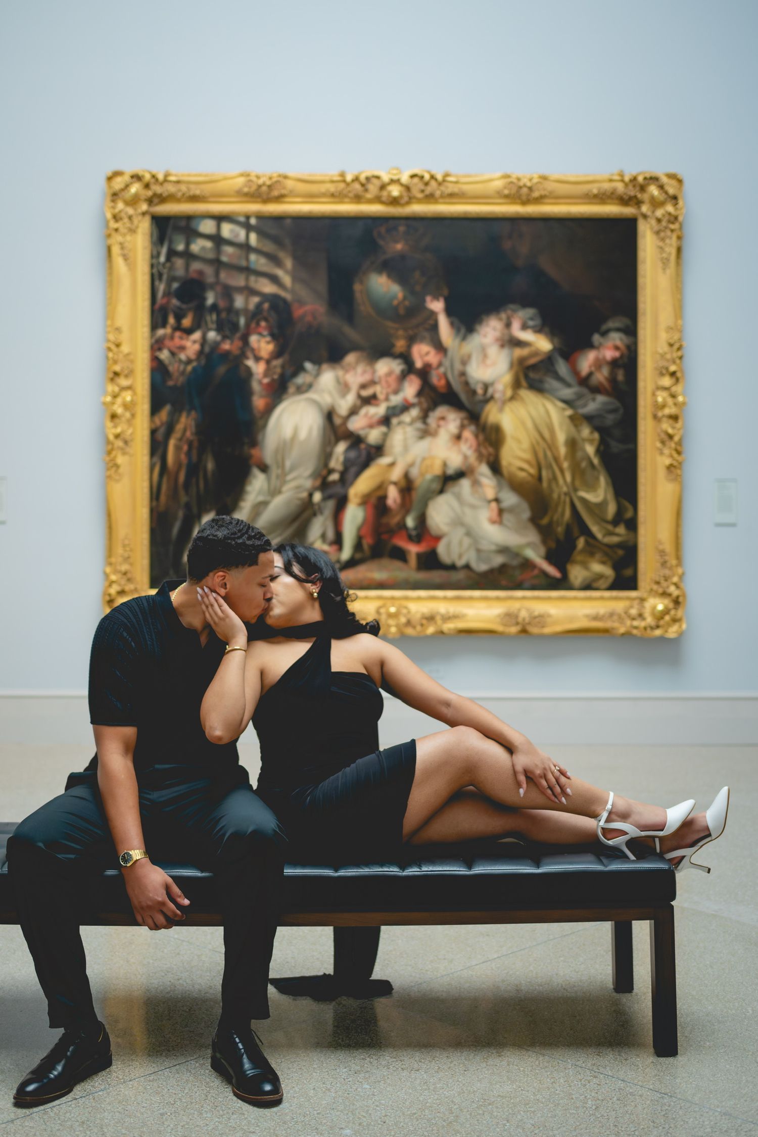 Artistic engagement photos of a couple lounging on a bench in an art gallery with classical paintings.