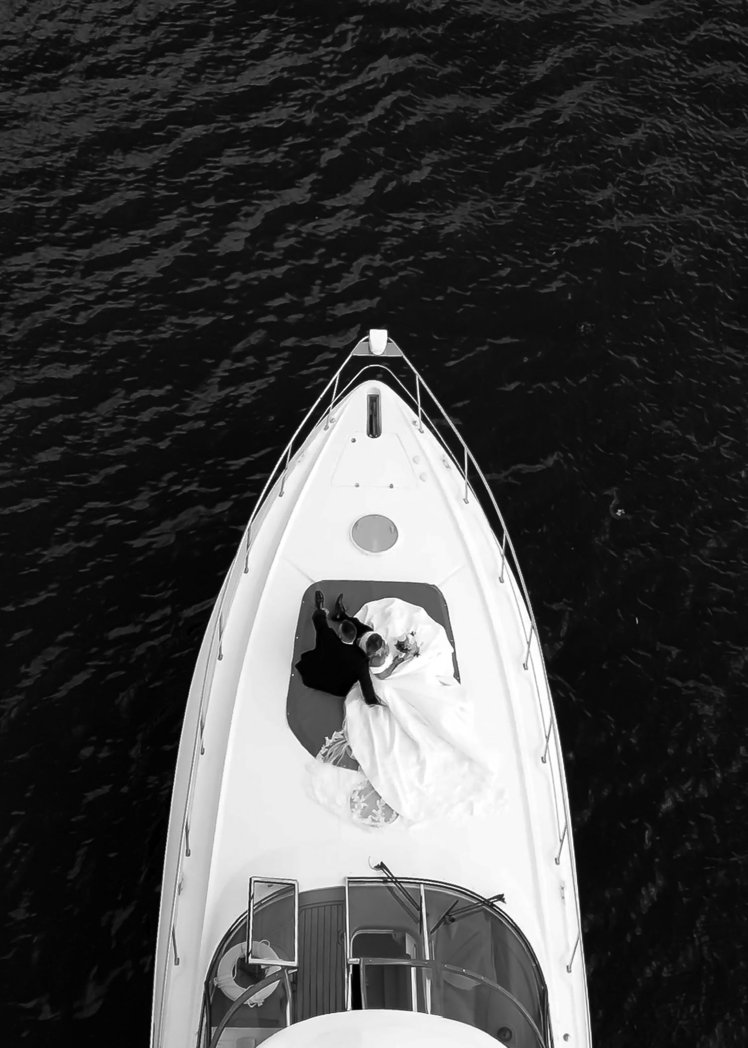 Overhead drone shot of bride in white dress on yacht deck in dark waters.