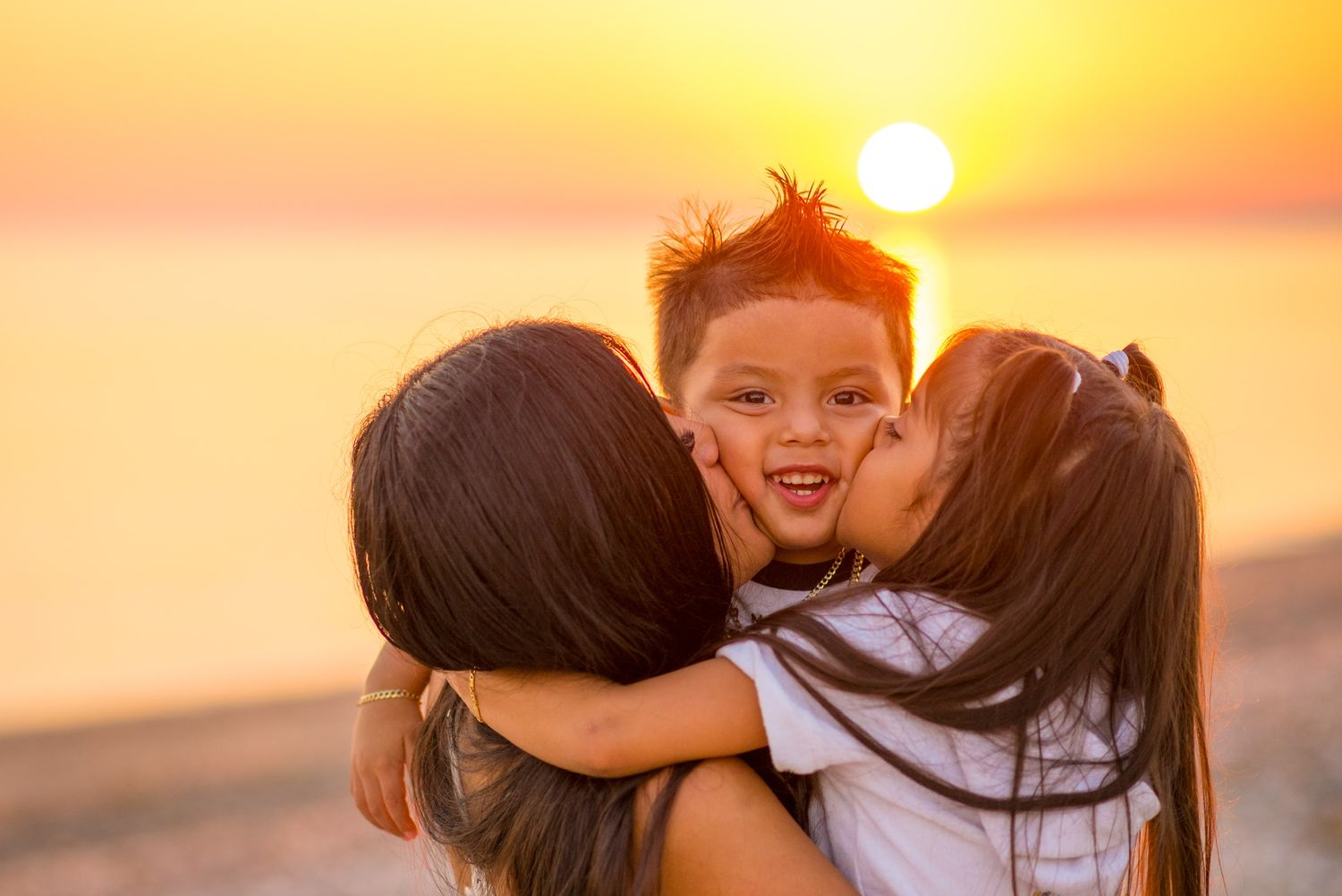 Family embracing against a vibrant orange sunset sky at the beach.