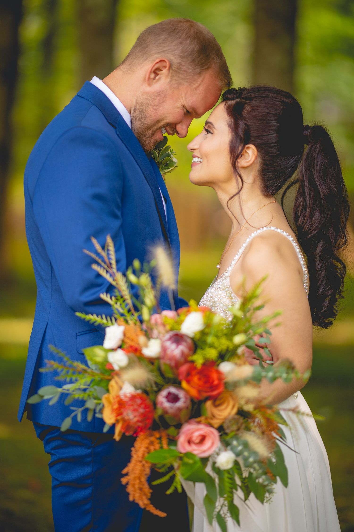 A vibrant autumn wedding bouquet features orange, pink and blue flowers against formal attire.