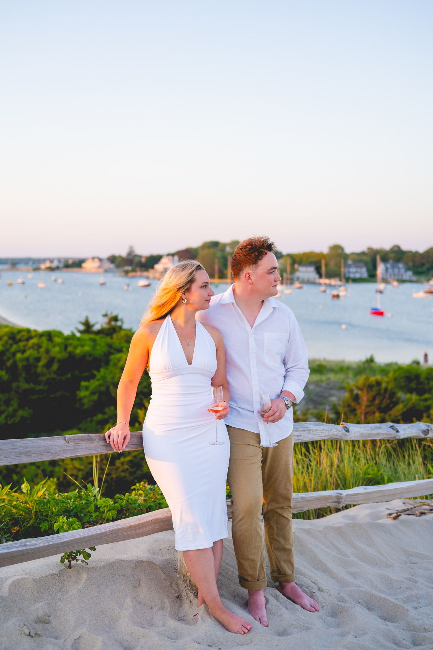 A couple sits together on sandy steps overlooking a harbor during sunset in Watch Hill, Rhode Island.