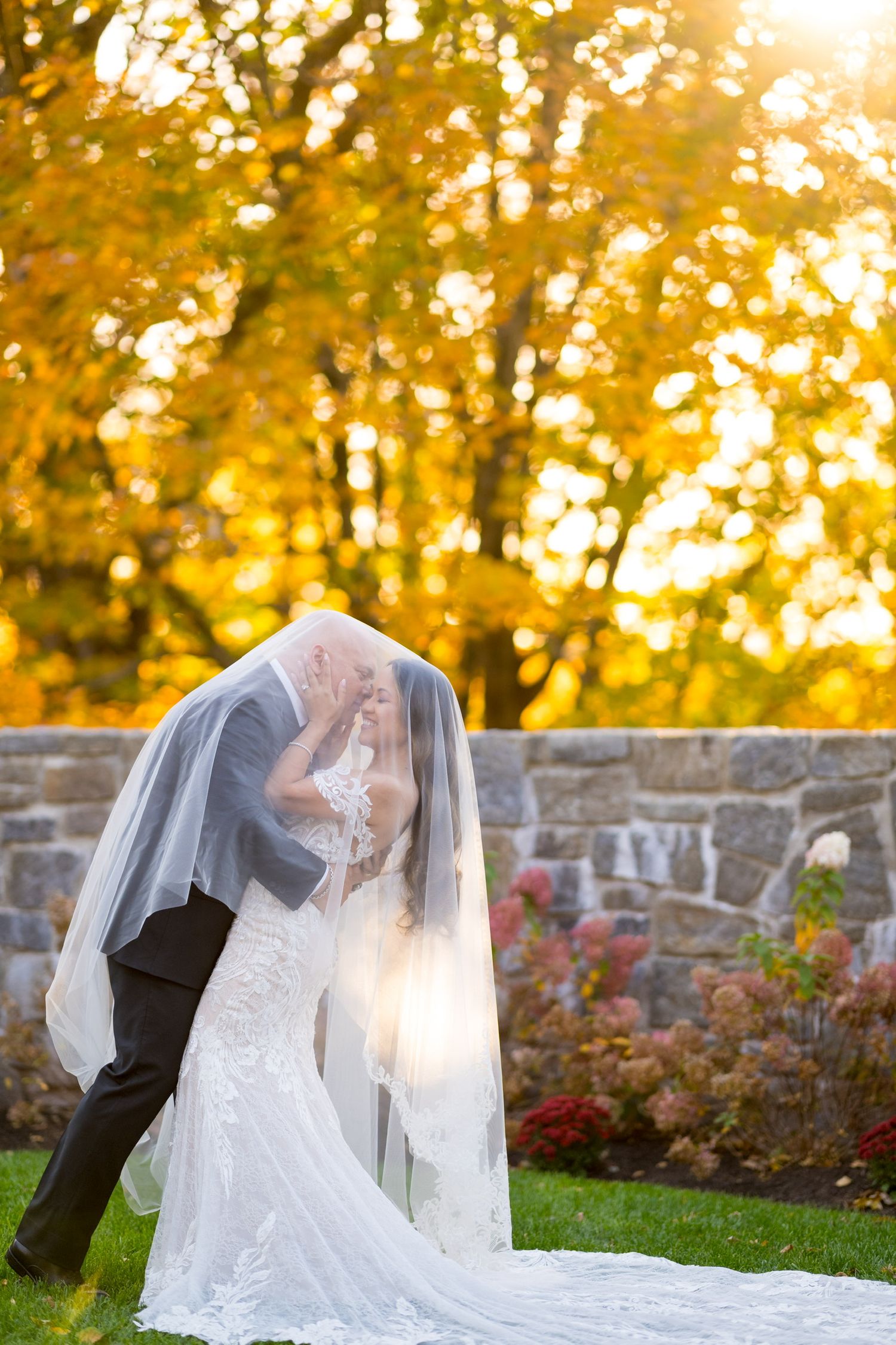 A couple in wedding attire shares an intimate moment against a backdrop of golden autumn trees at Le Chateau in Westchester County, New York