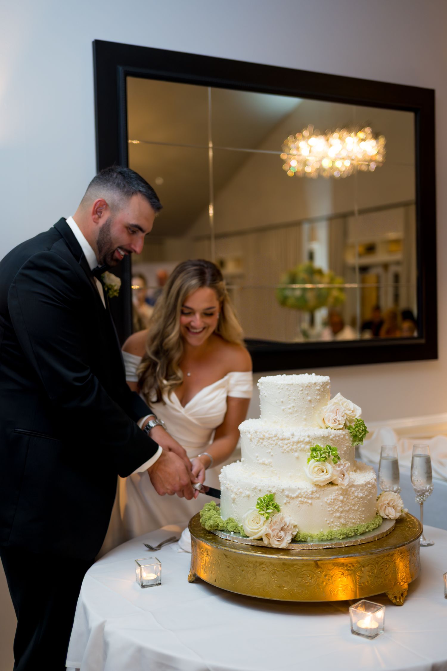 Wedding couple cutting their white tiered cake decorated with delicate green floral accents.