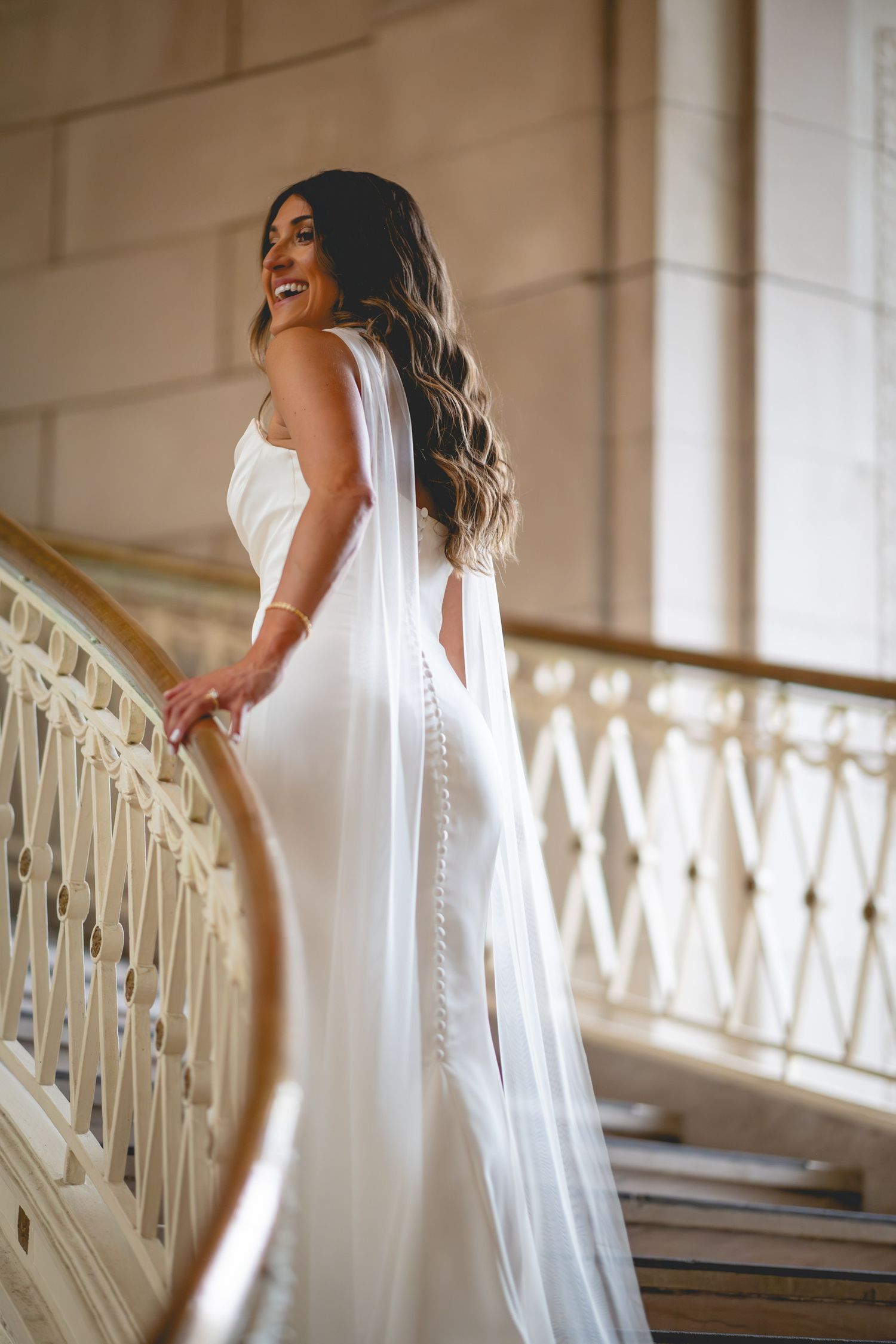 Bride in flowing white dress poses gracefully along an ornate indoor balcony railing at Hartford City Hall in Connecticut.