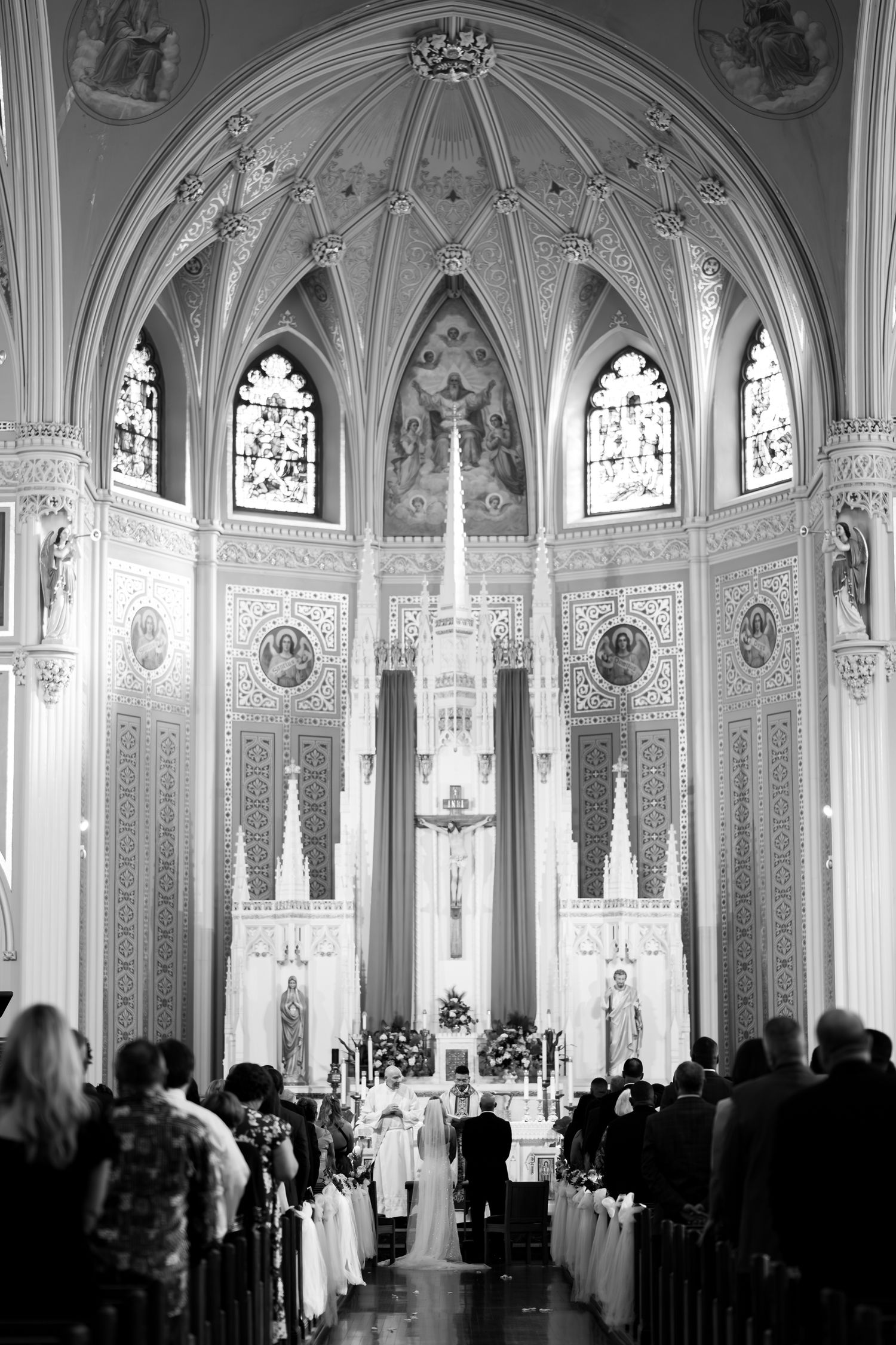 Gothic cathedral interior with vaulted ceiling and stained glass windows during wedding ceremony.