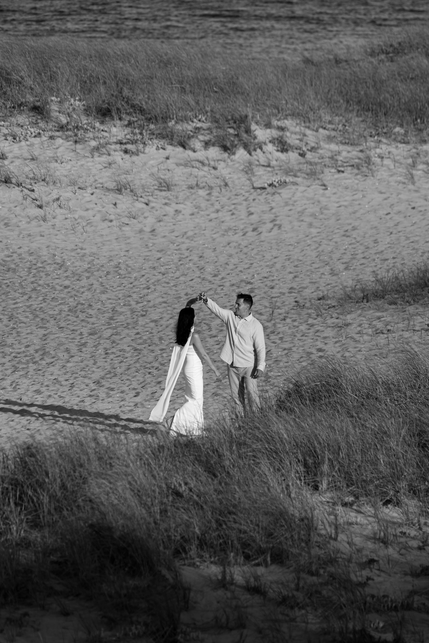 A black and white aerial view of a couple walking through coastal dunes and beach grass in Chatham, Massachusetts