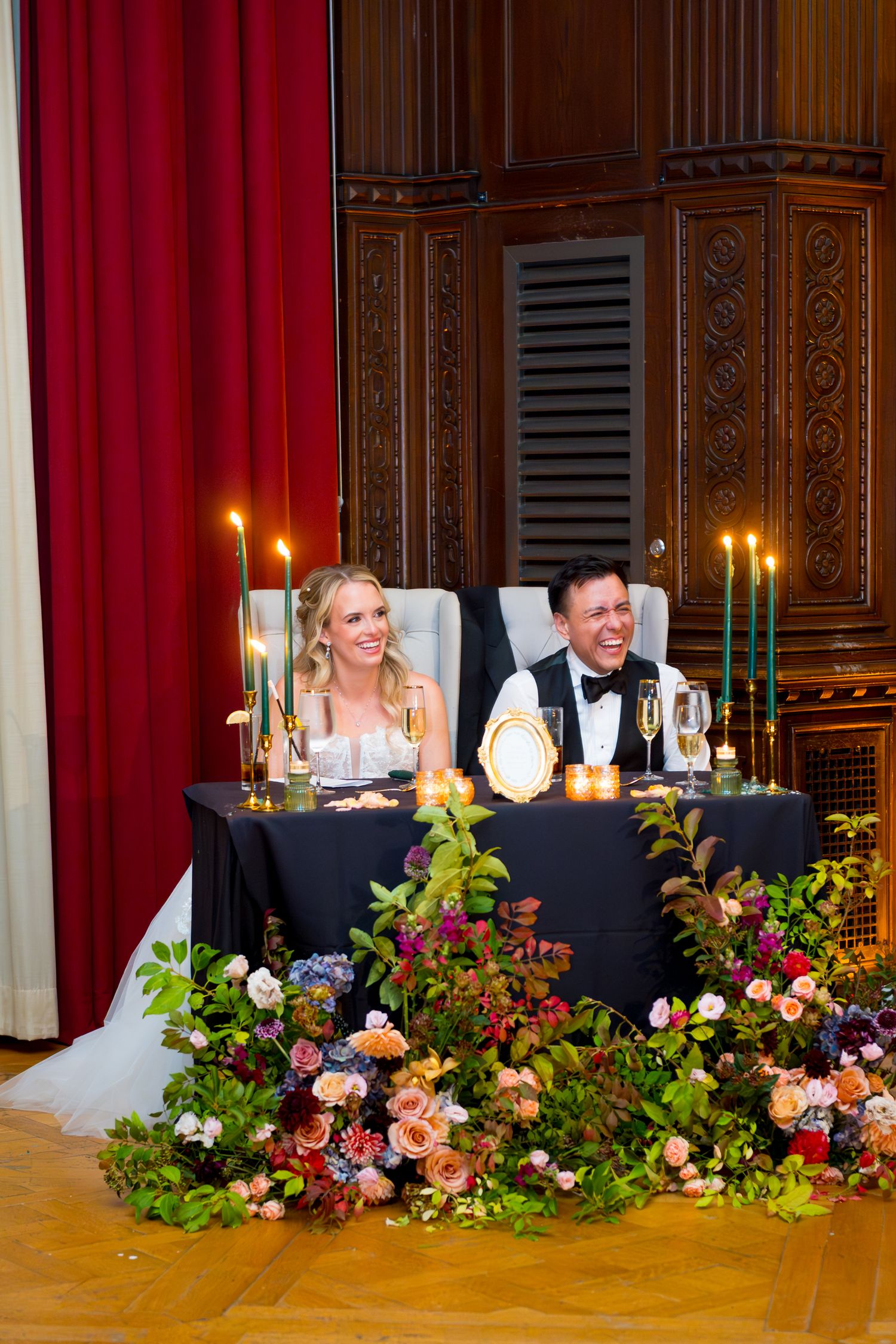 Elegant wedding head table decorated with lush floral arrangements and glowing candles in an ornate ballroom.
