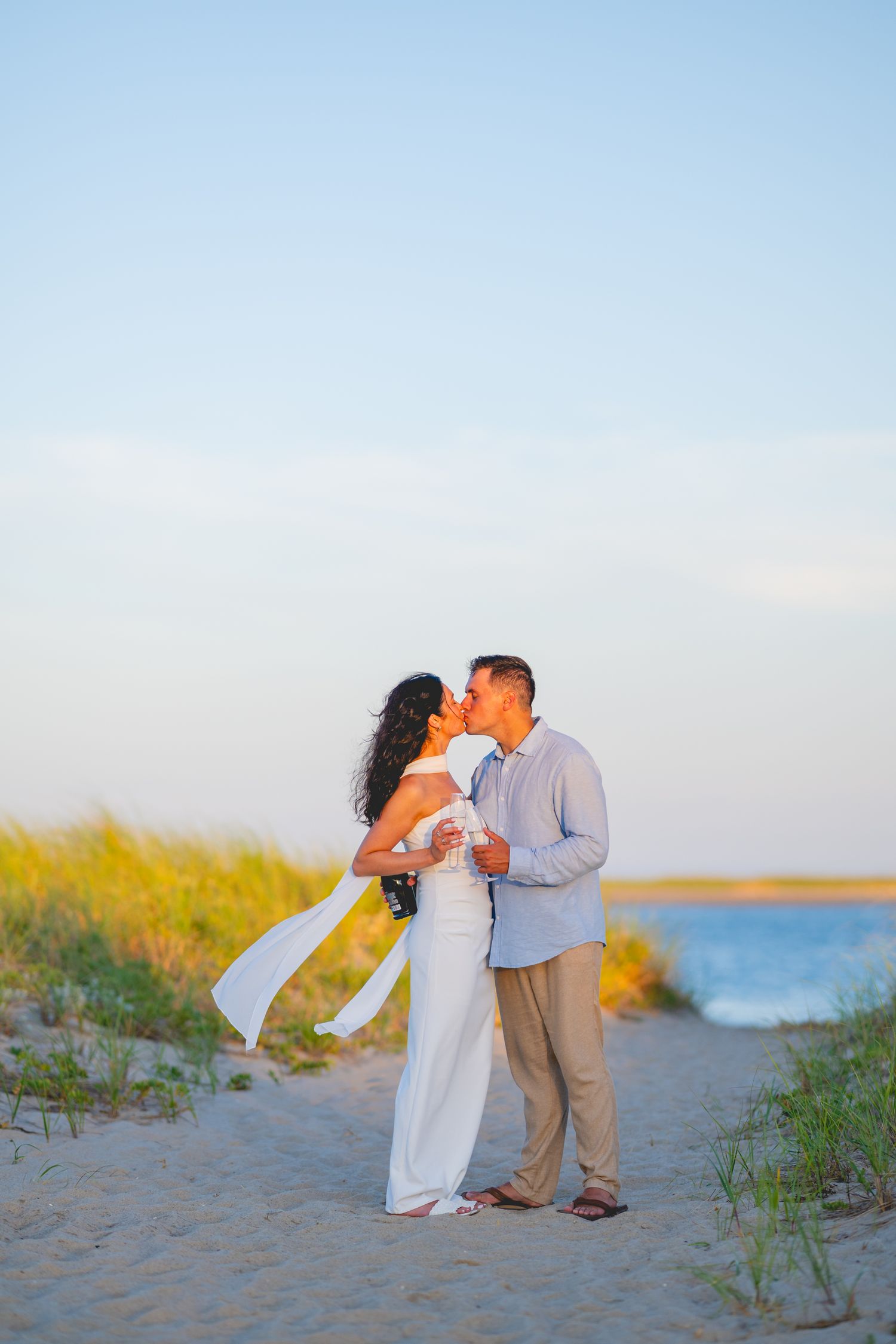 A romantic moment between a couple on a coastal Cape Cod path with ocean and beach grass in the background.