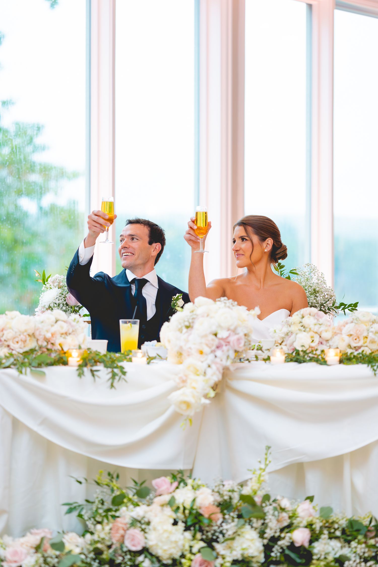 Newlyweds raise champagne glasses at reception with floral decorated head table.