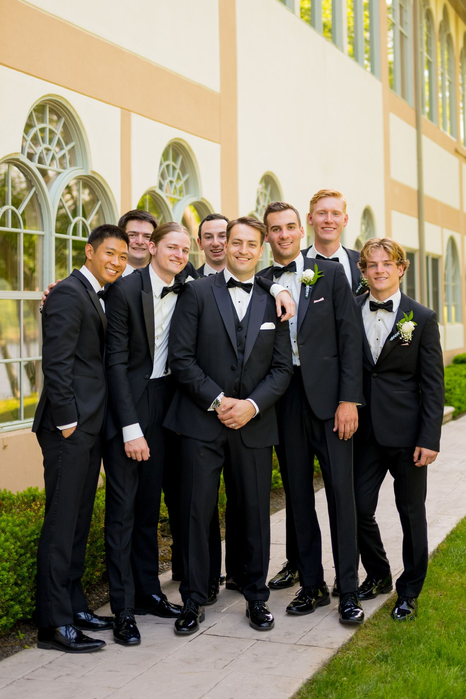 Groomsmen in black tuxedos pose together for formal wedding party photo.