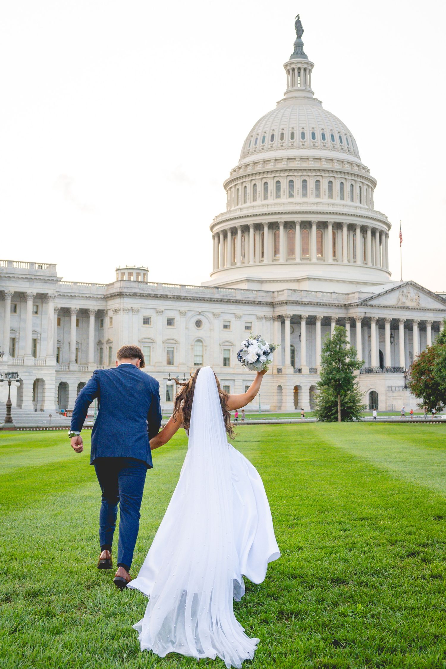 Wedding couple playfully runs across the lawn in front of the majestic US Capitol building.