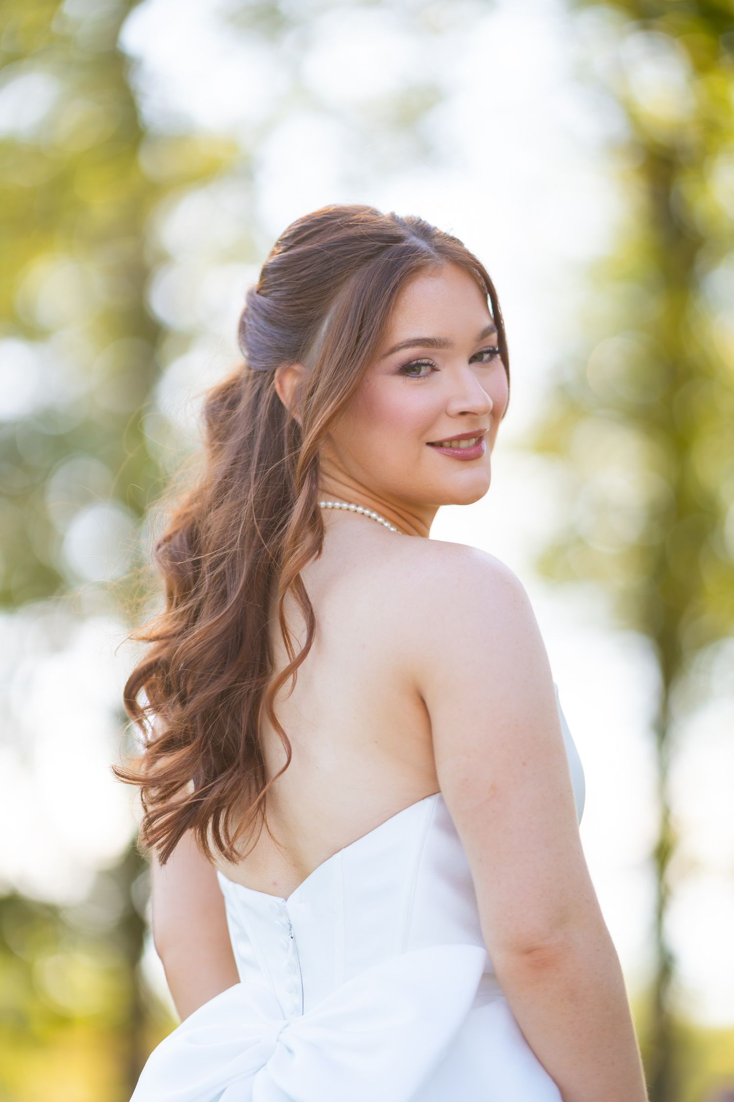 Bride poses in white wedding gown against soft natural outdoor lighting.