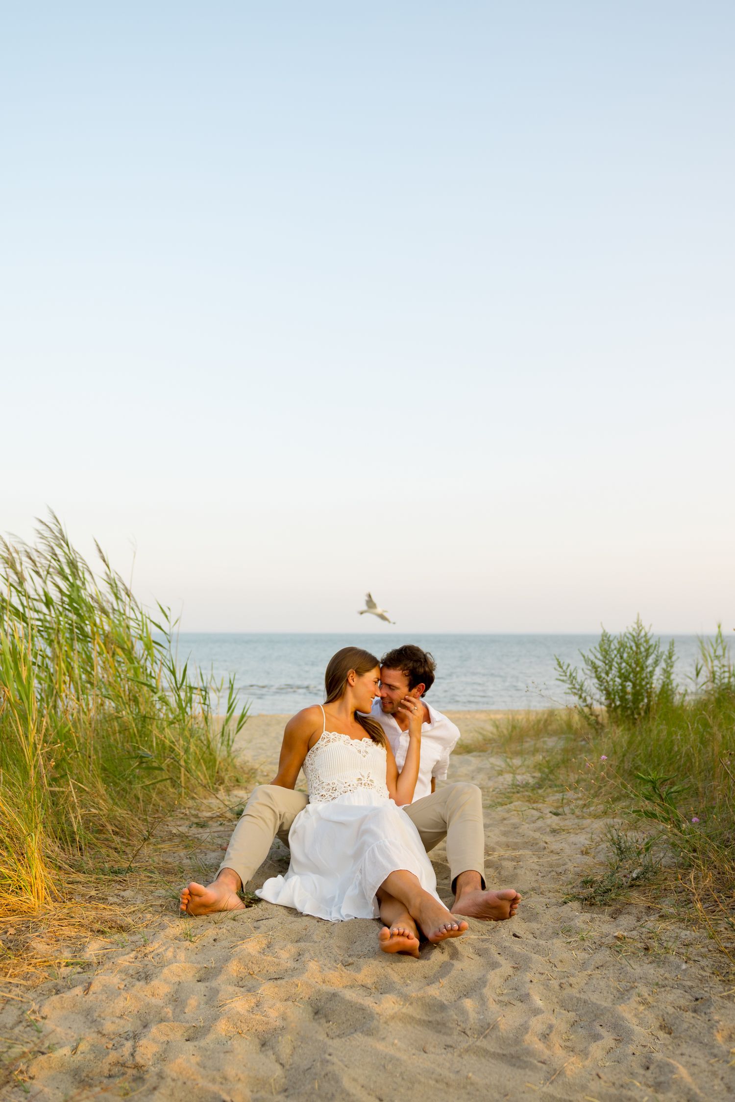 Romantic couple sitting together on sandy beach path with ocean view.