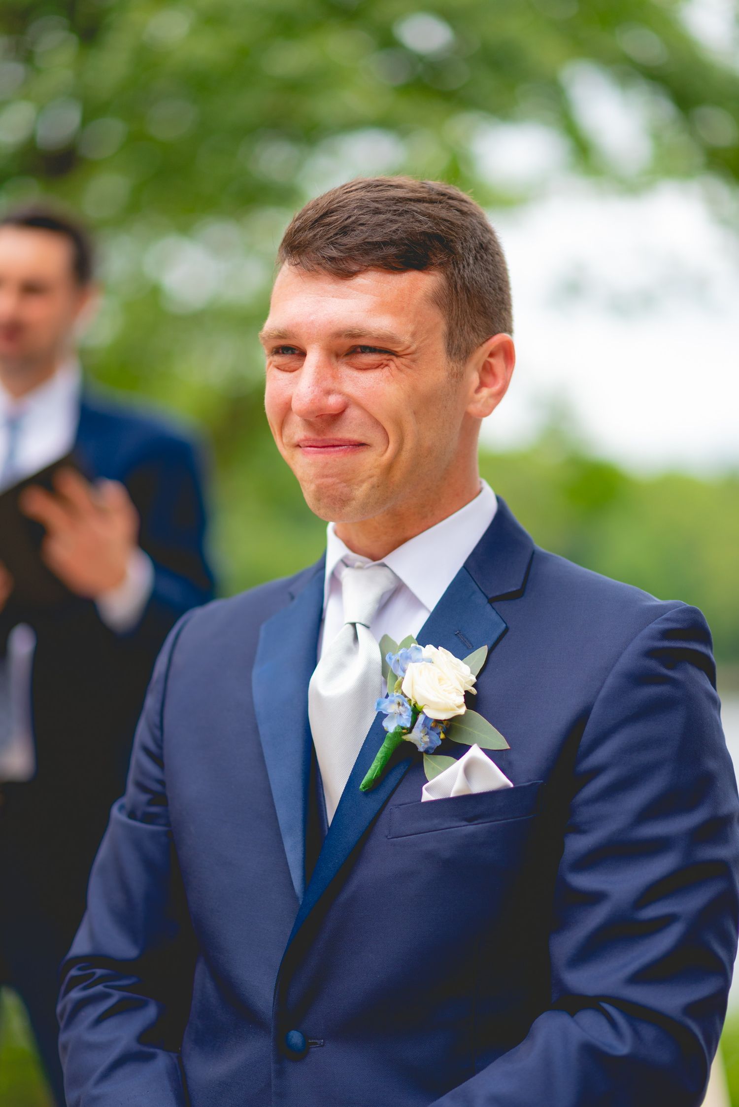 Groomsmen in navy suits share a joyful moment during outdoor wedding ceremony.