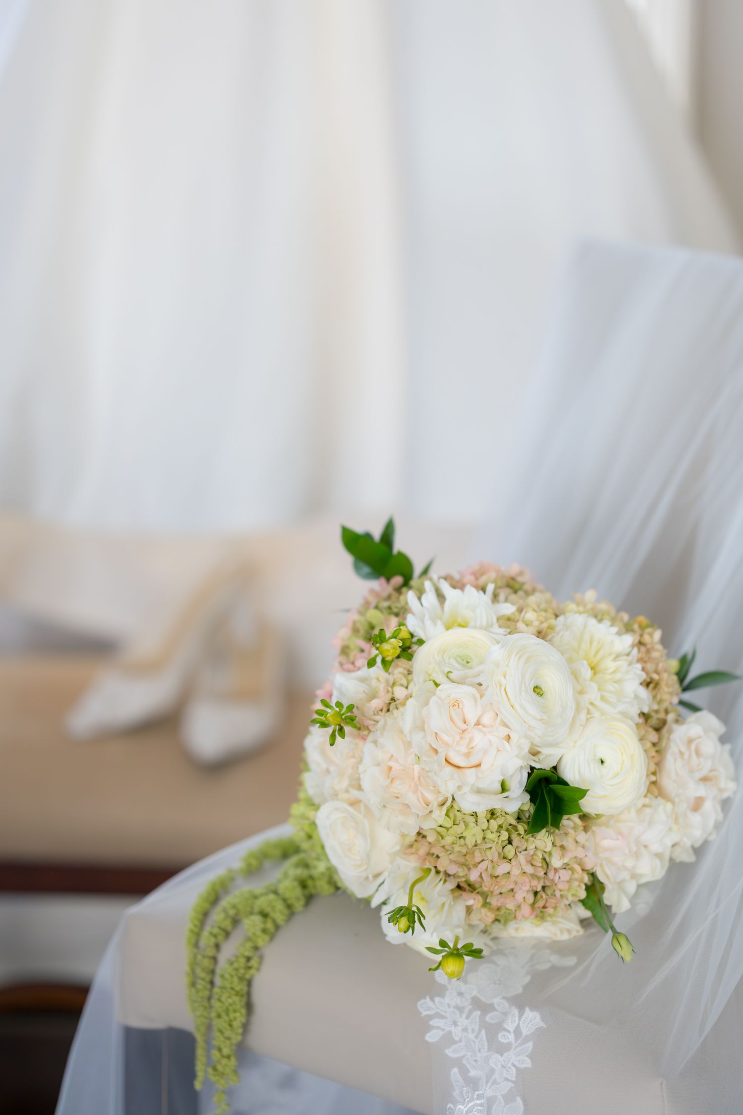Delicate white and blush floral arrangement with greenery against a light background.