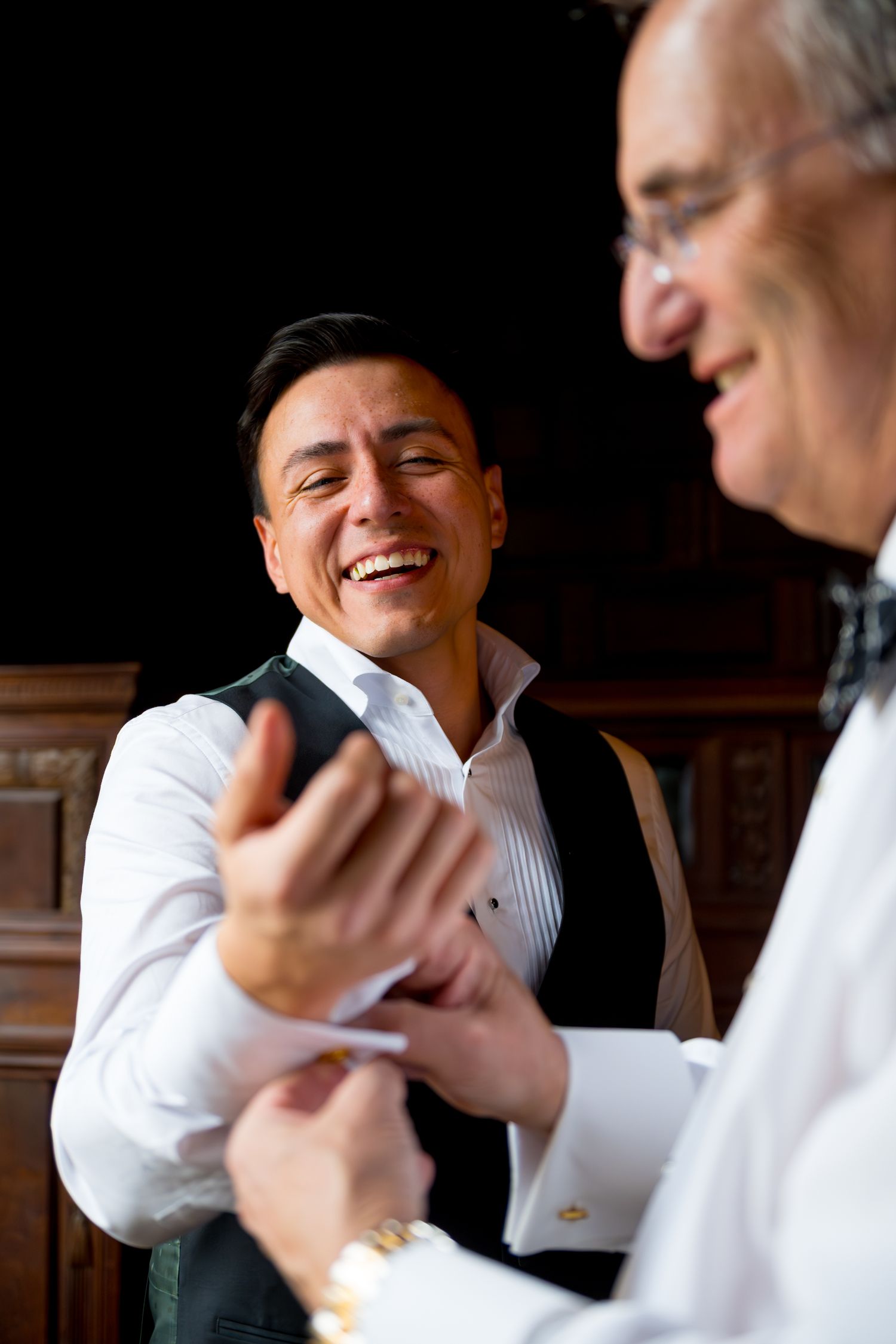Two men in formal attire share a candid laughing moment during a wedding celebration.
