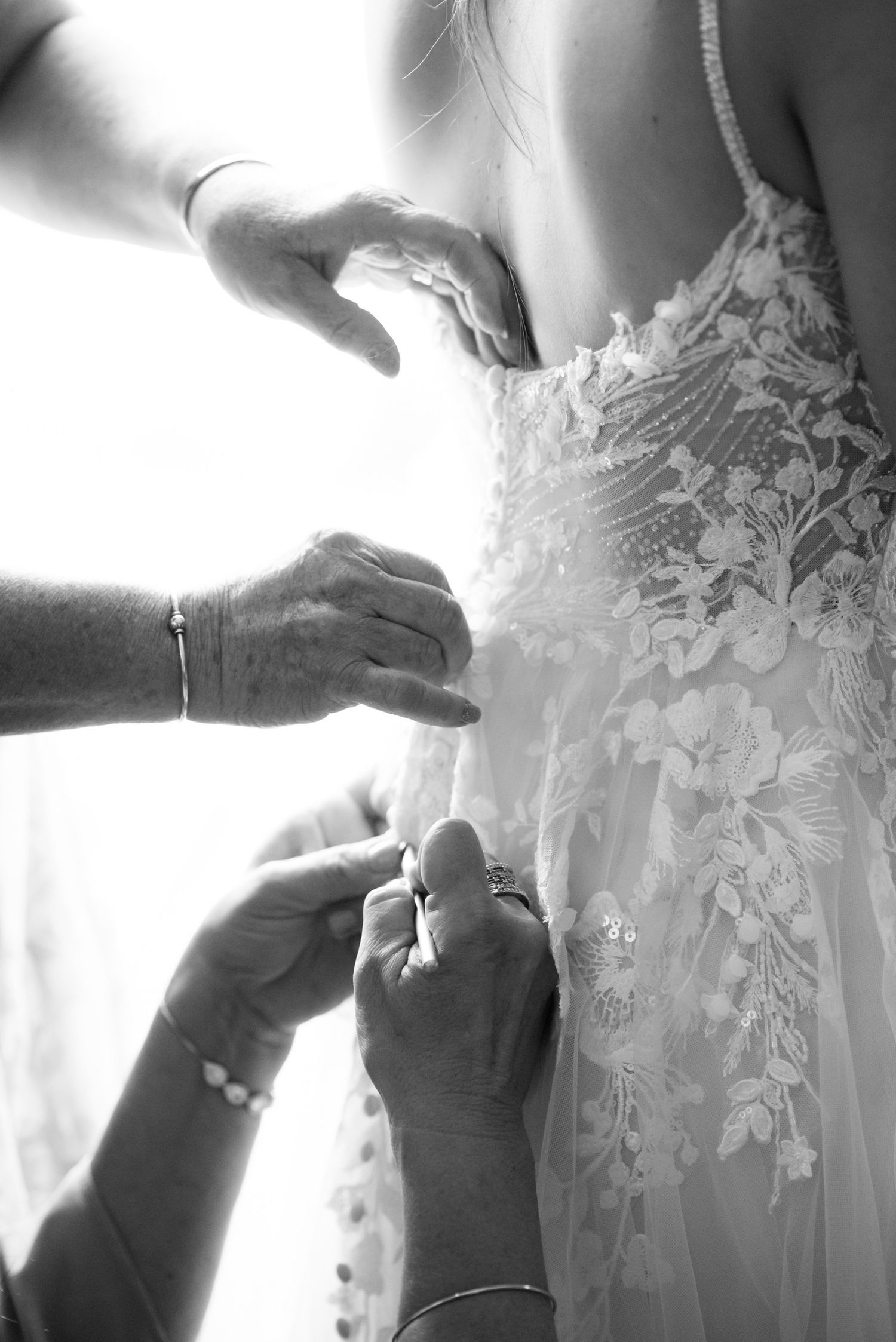 Close-up details of lace wedding dress being adjusted in black and white.
