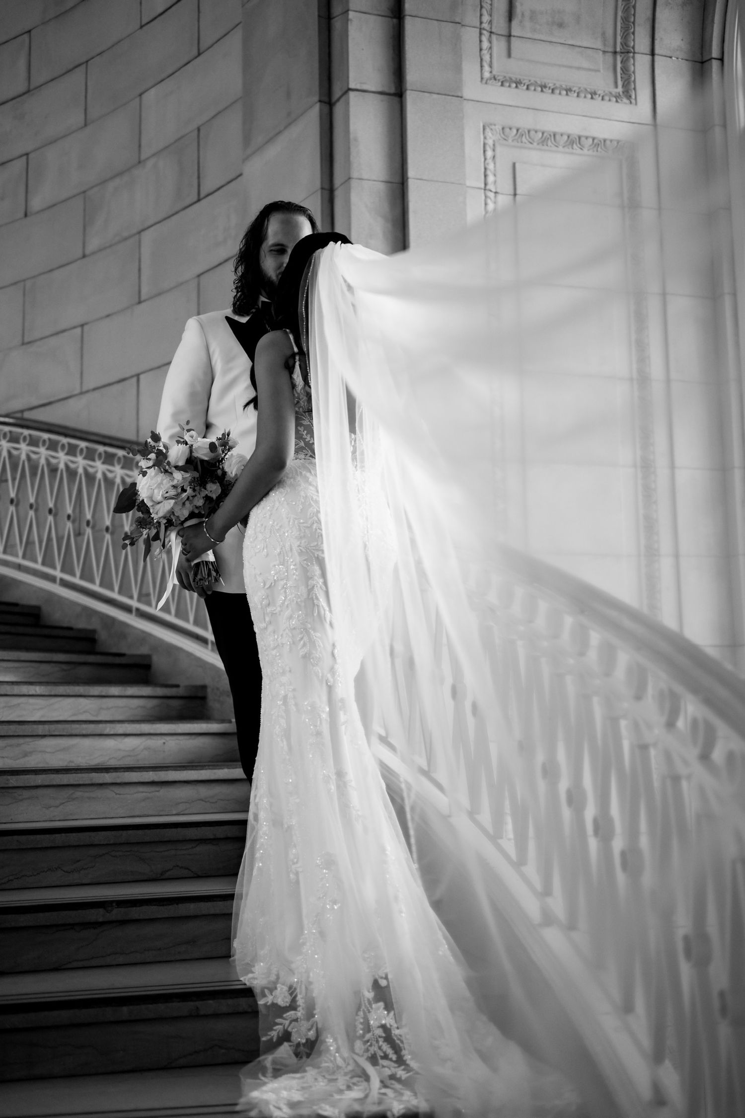 Wedding dress train cascades down grand staircase in dramatic black and white.