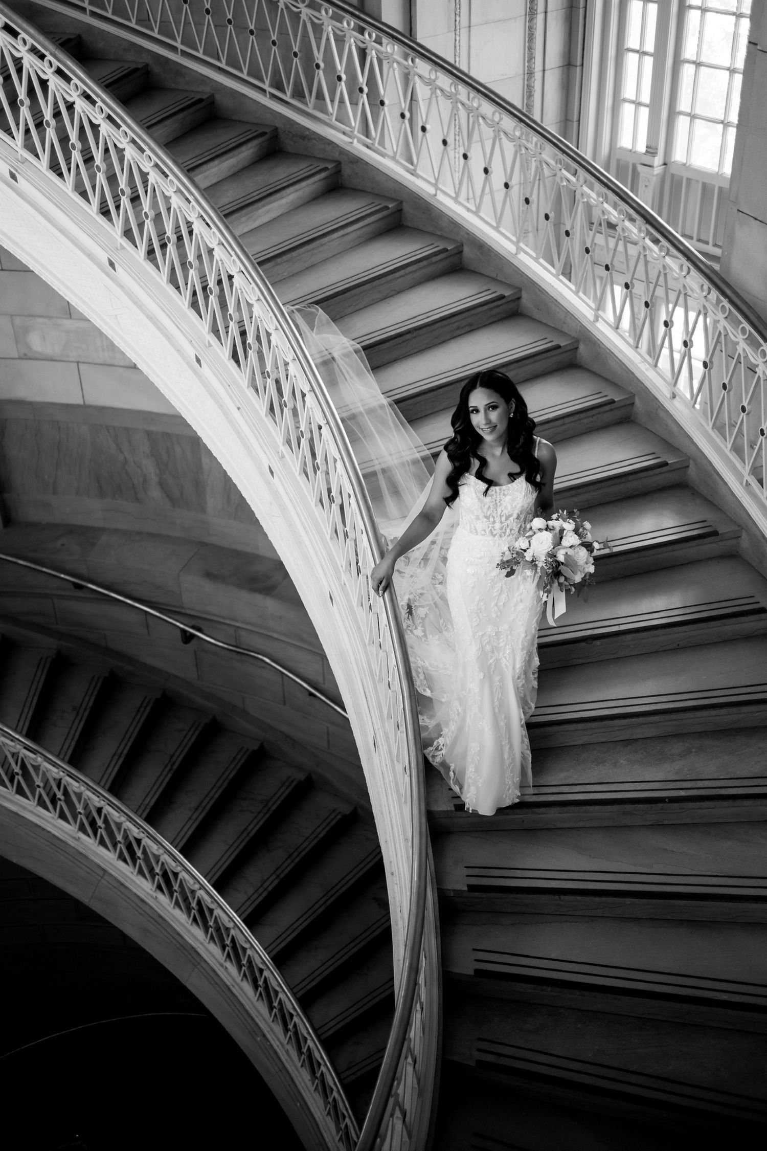Dramatic black and white photo of a wedding dress flowing down curved stairs.