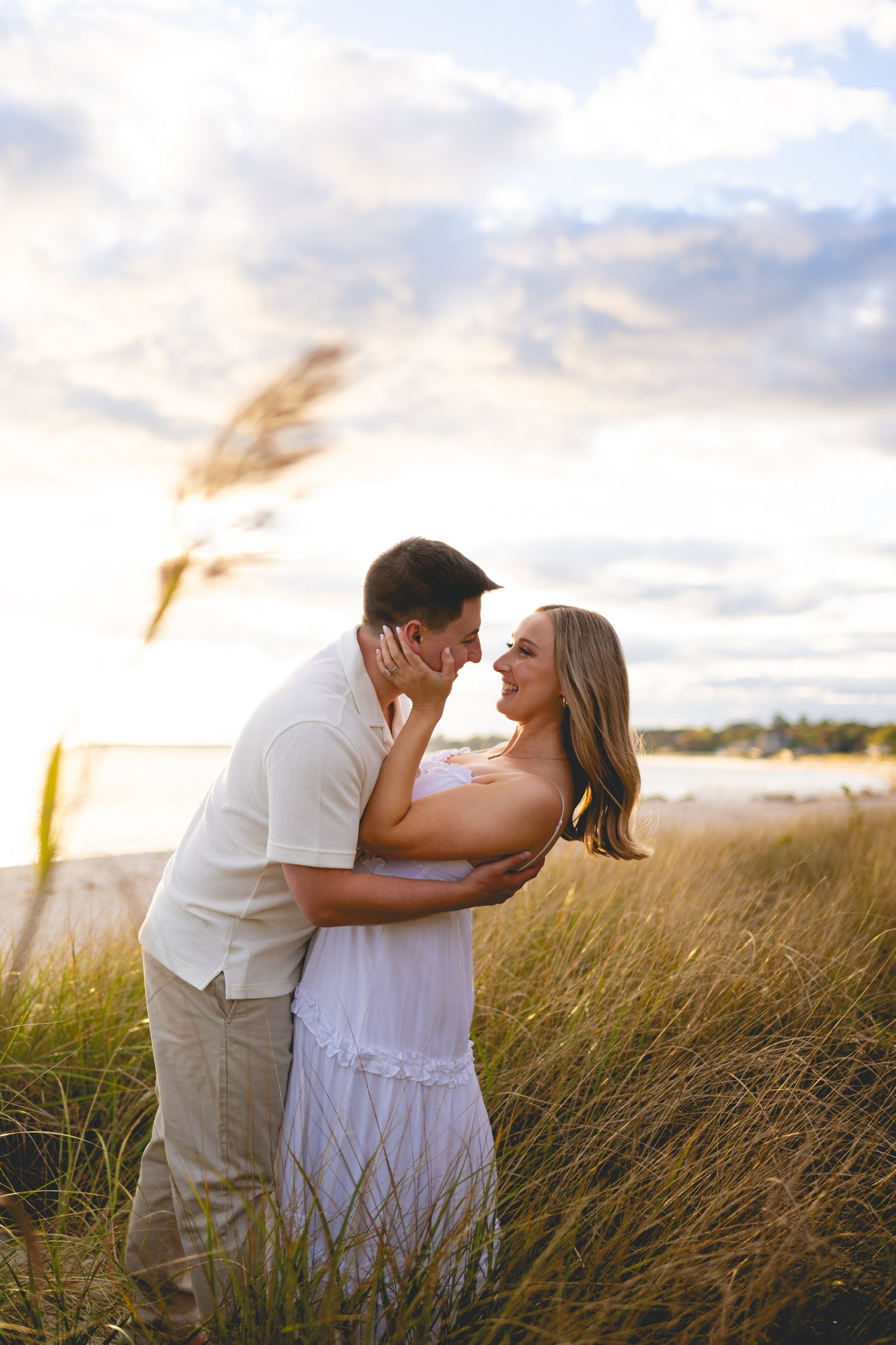 Tender moment between couple against sunset and beach grass at Harkness Memorial State Park in Waterford, Connecticut.