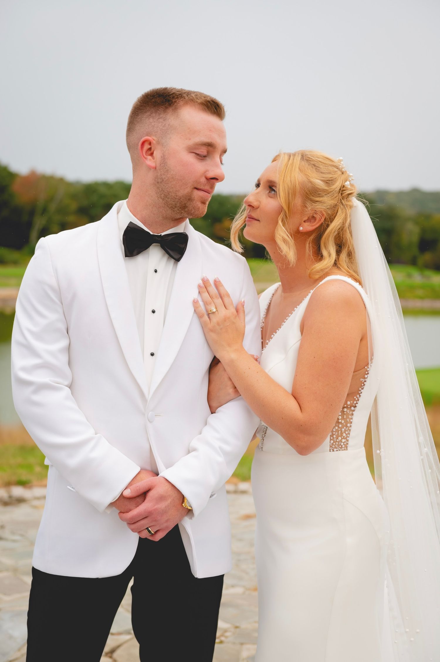 Romantic wedding couple in formal attire share intimate moments against a natural outdoor backdrop.