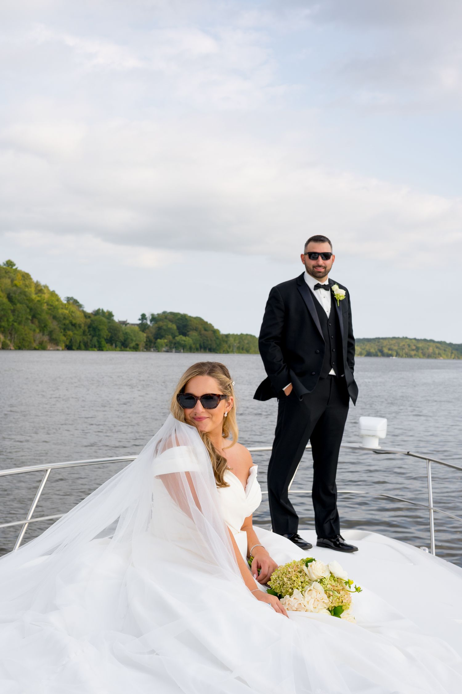 Stylish wedding couple poses on yacht deck with waterfront backdrop.