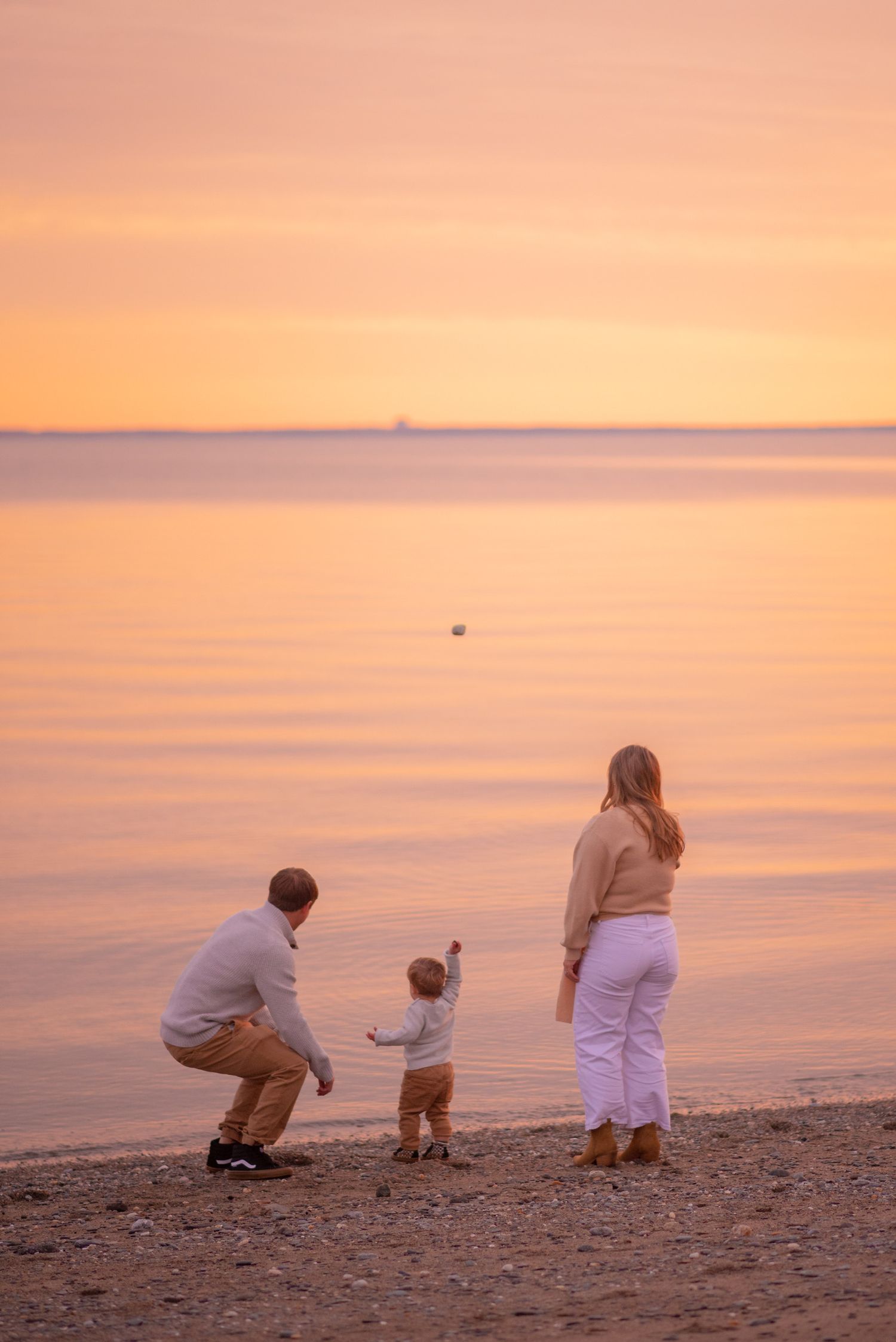 Family sits together on a beach during a peaceful sunset over calm waters.