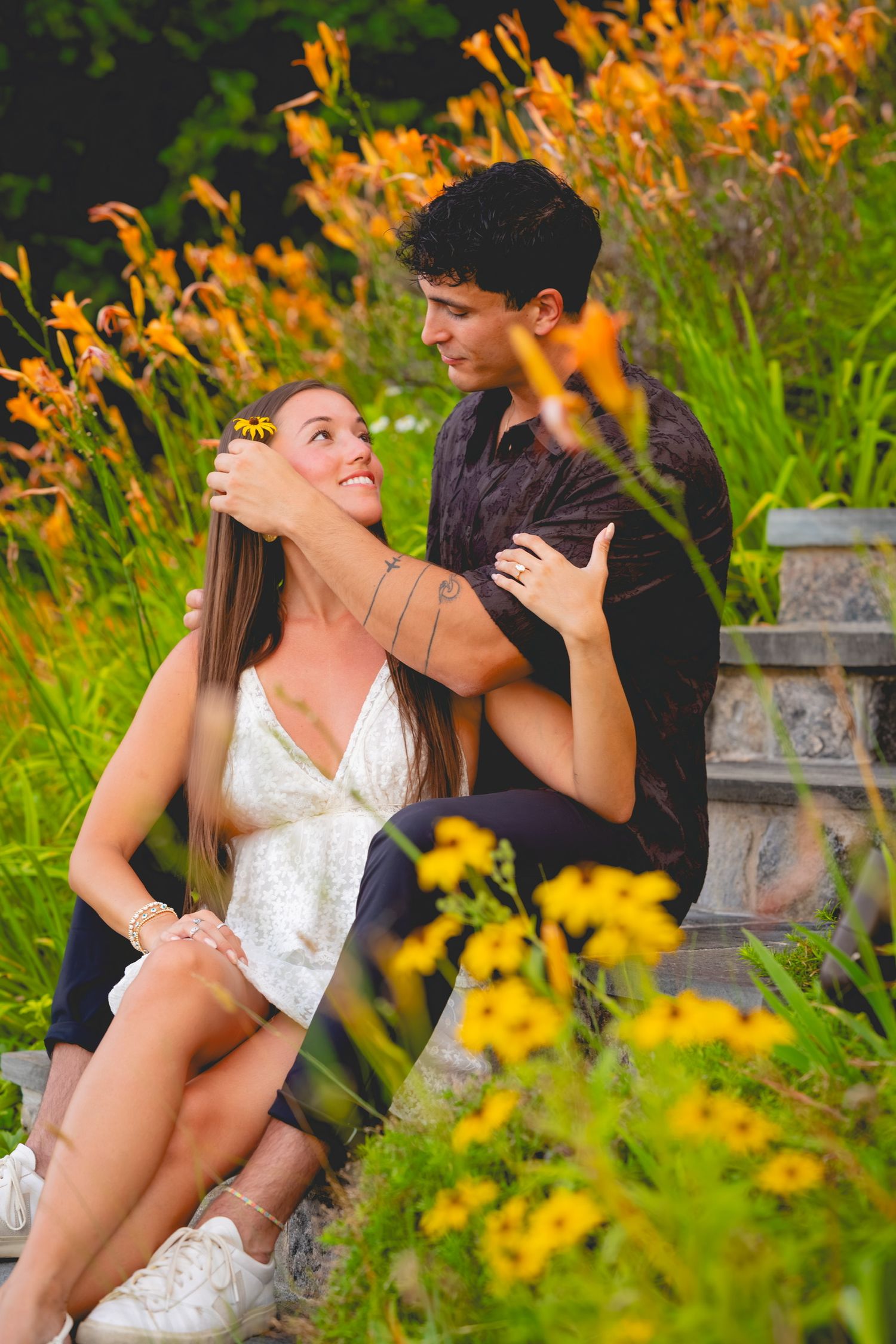 Playful couple posing among vibrant orange daylilies in a garden setting on Candlewood Lake in Connecticut.