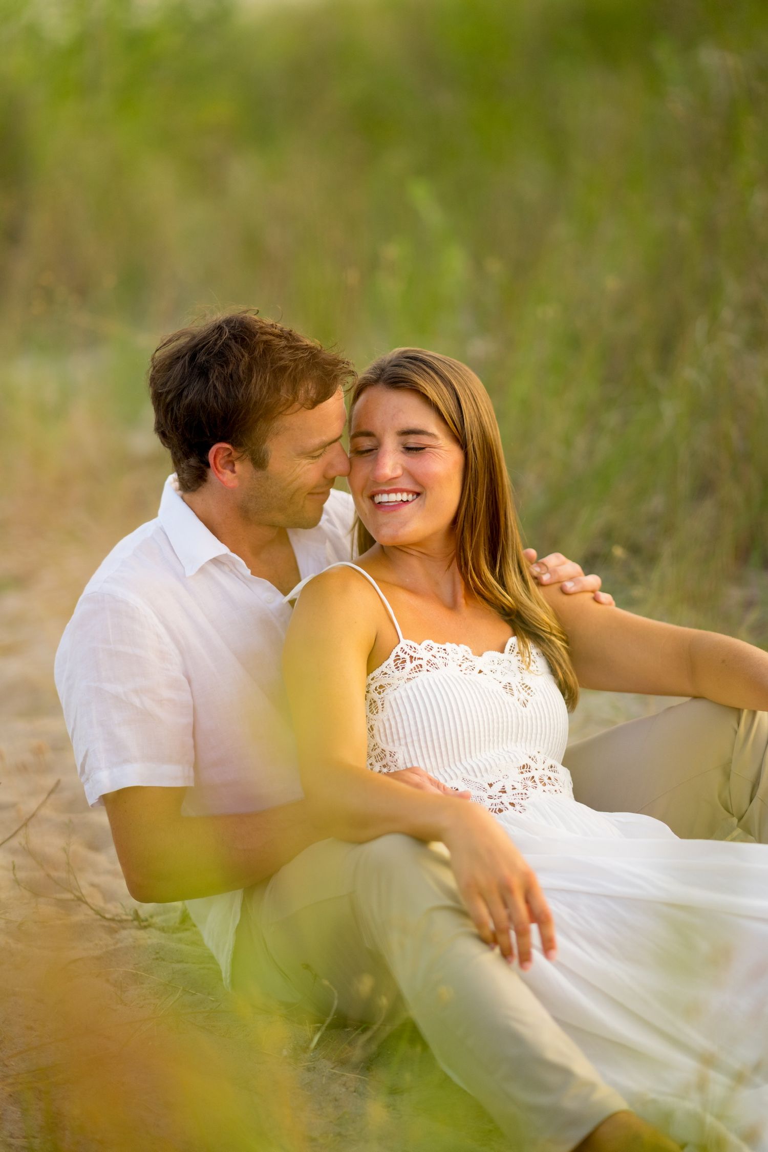 Couple in white clothing sharing romantic moments in tall grass during golden hour in Westport, Connecticut.