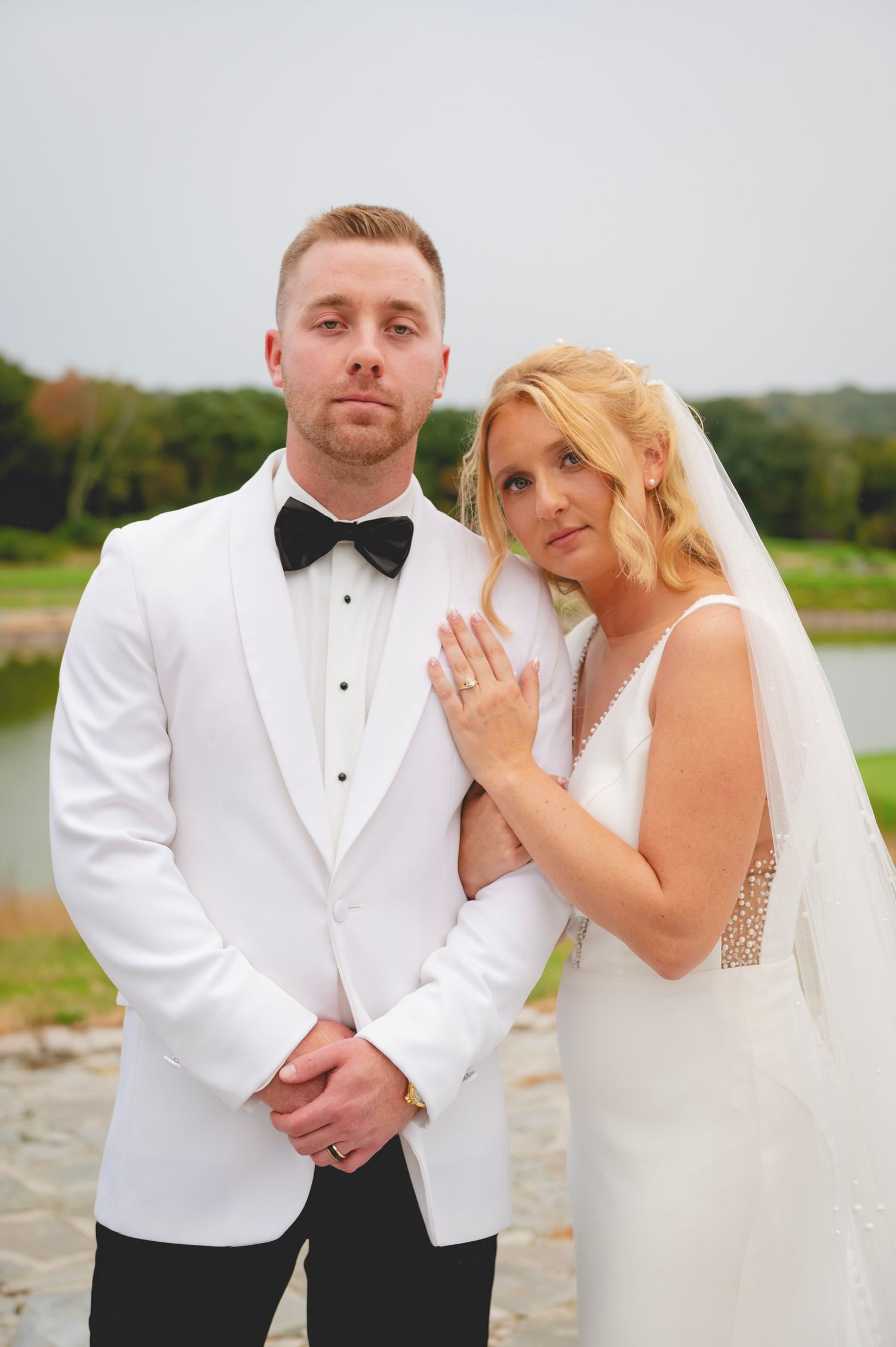 Elegant wedding portrait with couple in white tuxedo and bridal gown by waterfront.