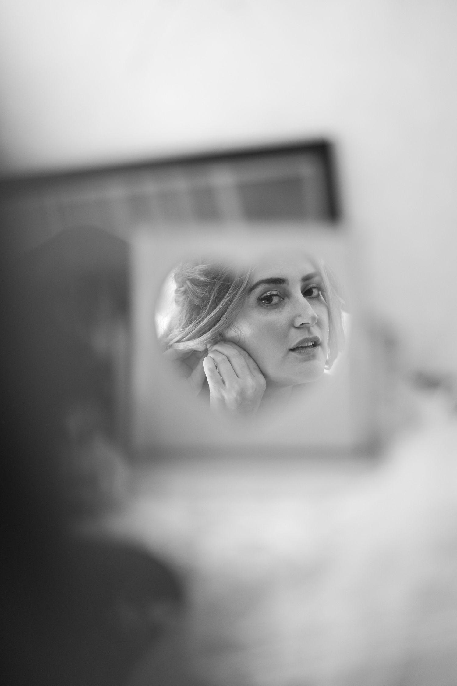 Artistic black and white reflection shot through mirror during wedding preparations.