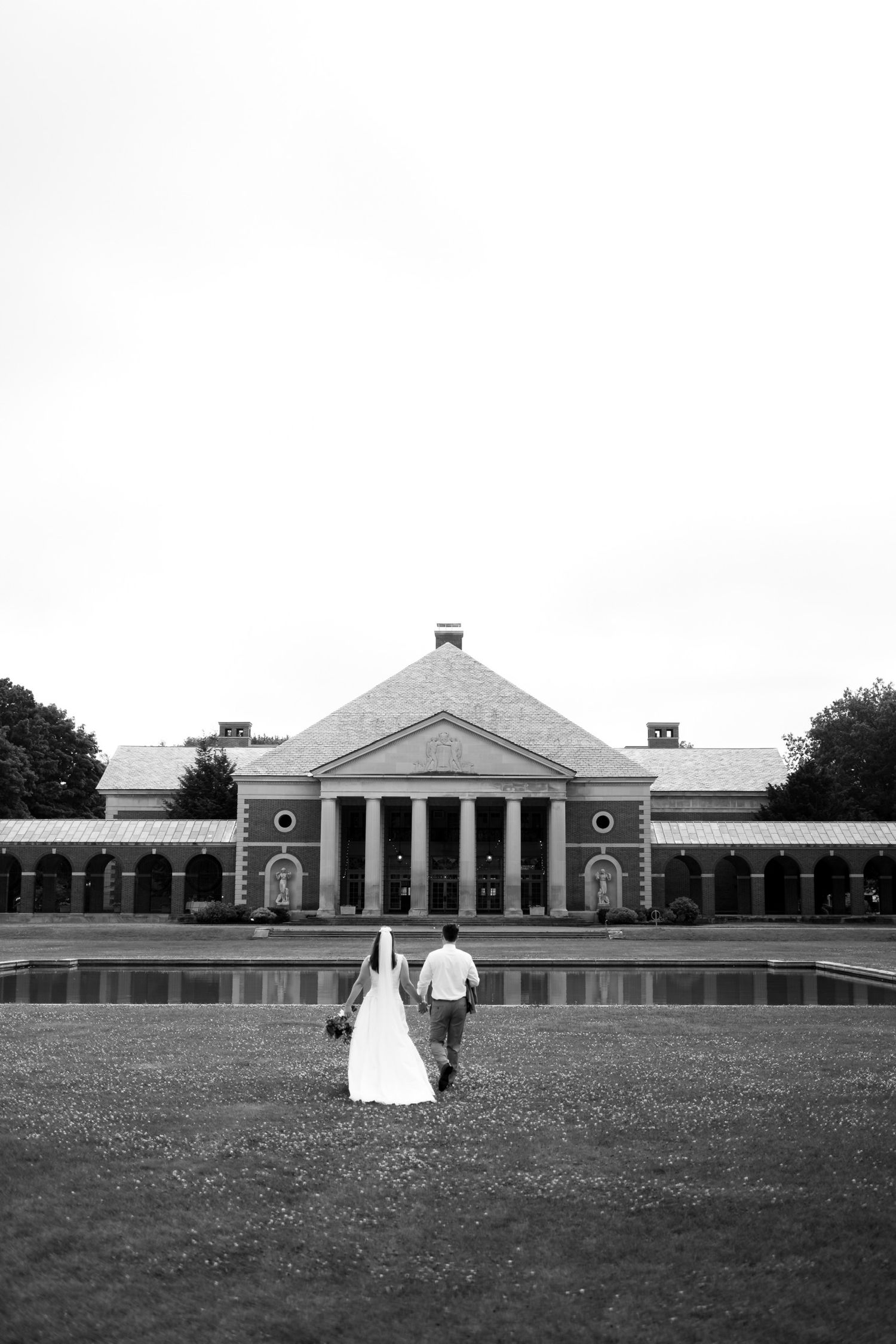 Black and white landscape of neoclassical building with wedding couple in distance.
