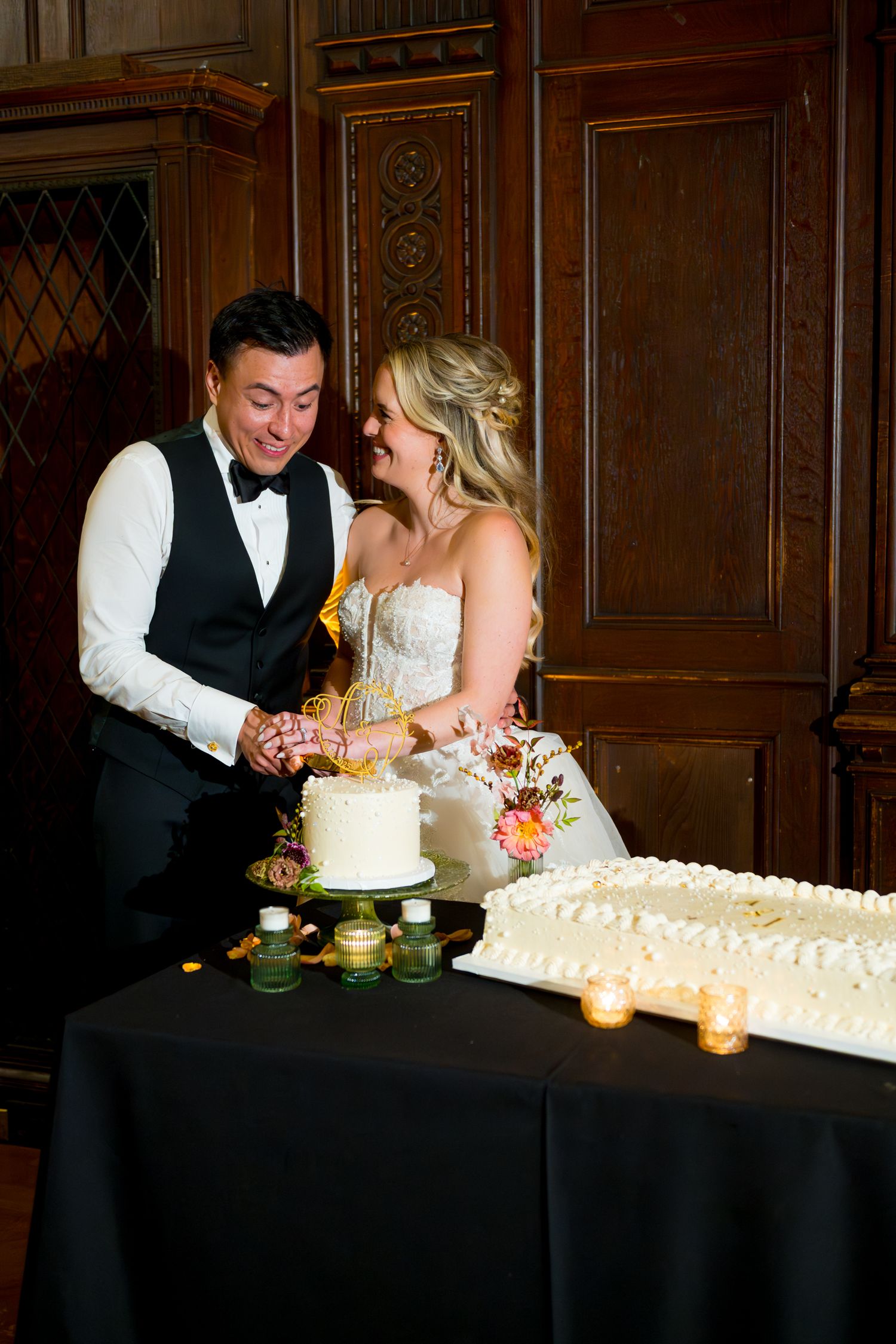 A couple shares an intimate moment while cutting their elegant wedding cake in a dimly lit reception venue.