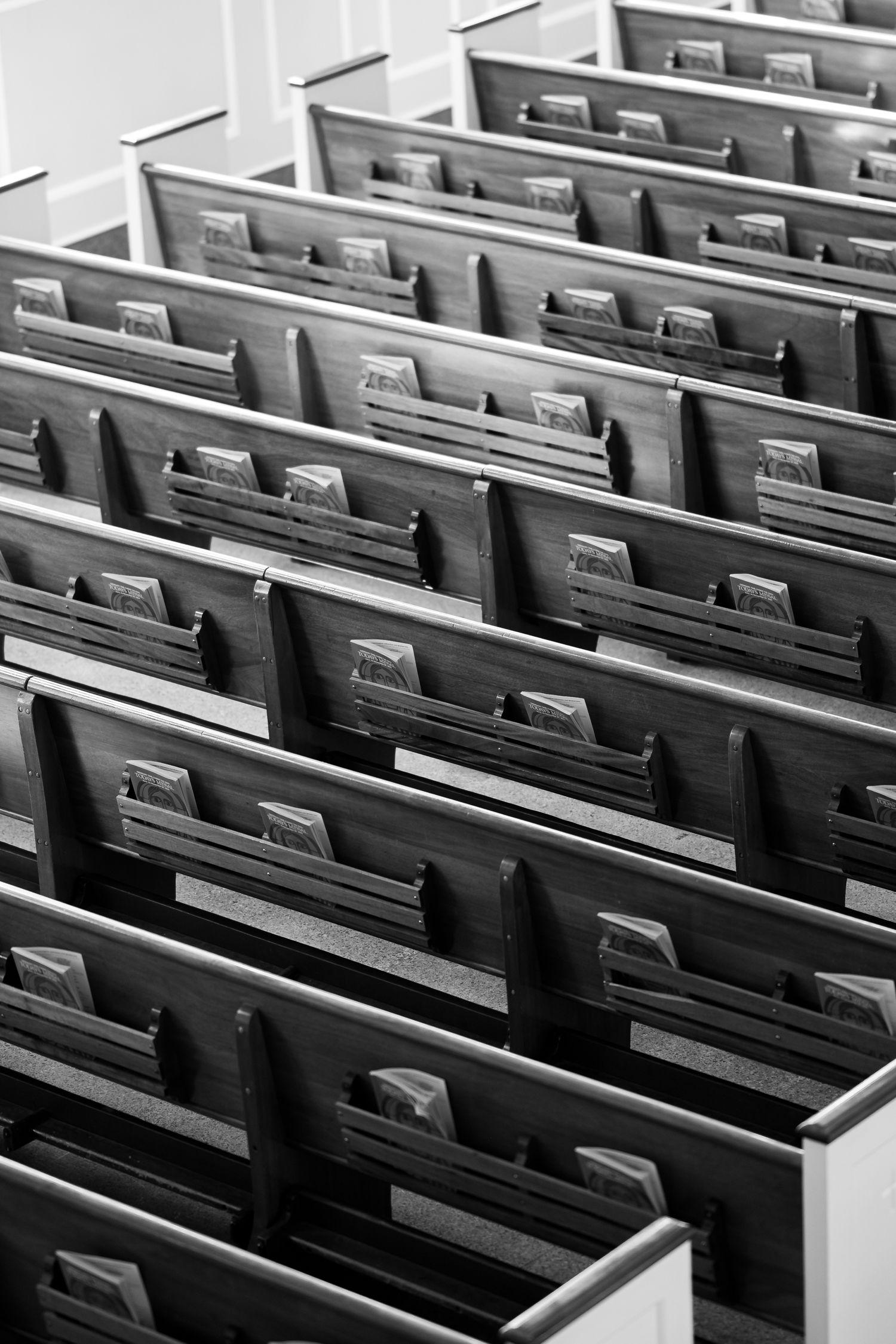 Empty wooden church pews arranged in rows create a symmetrical pattern in black and white.