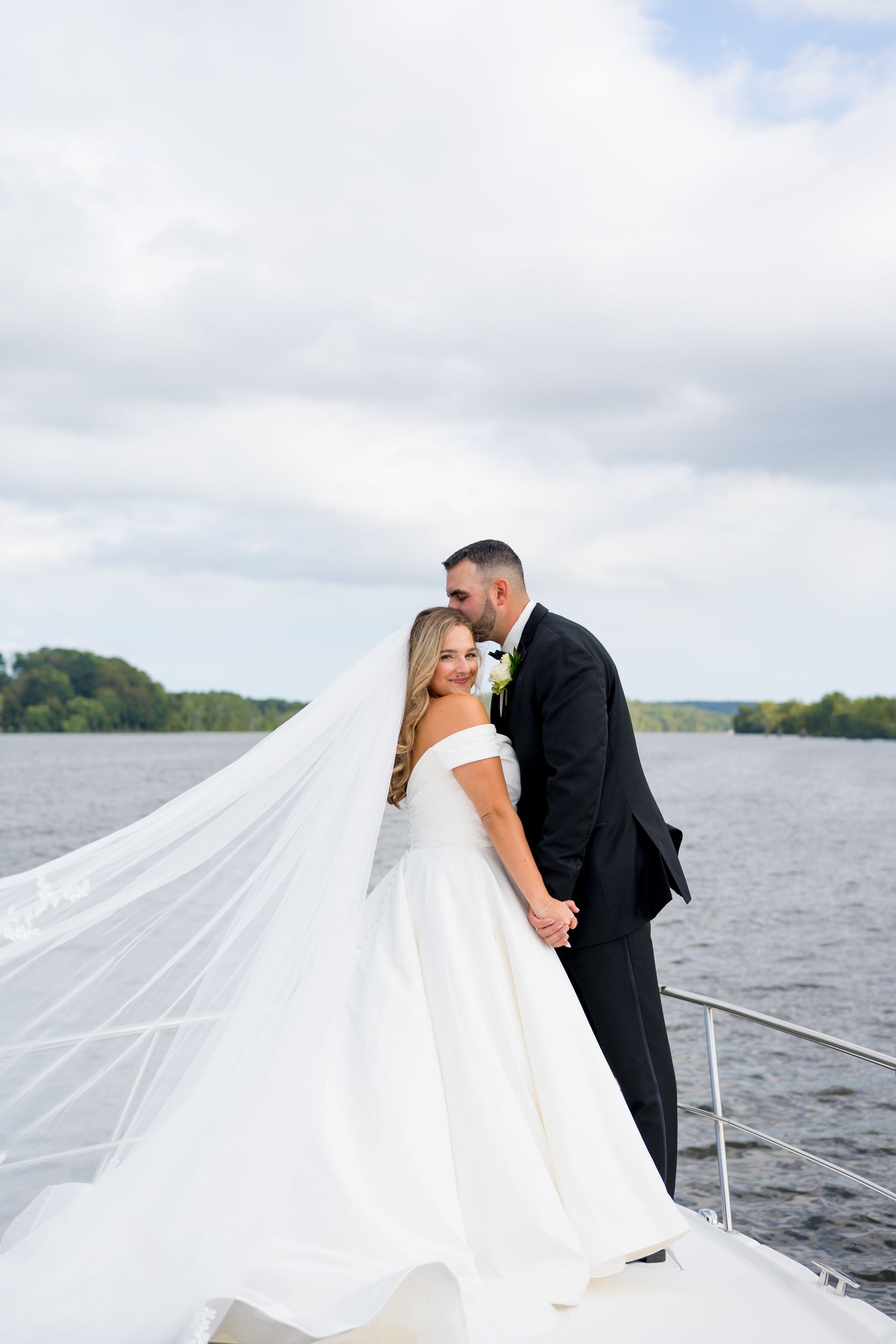 Newlyweds sharing intimate moments on a boat deck with flowing white veil in the breeze.