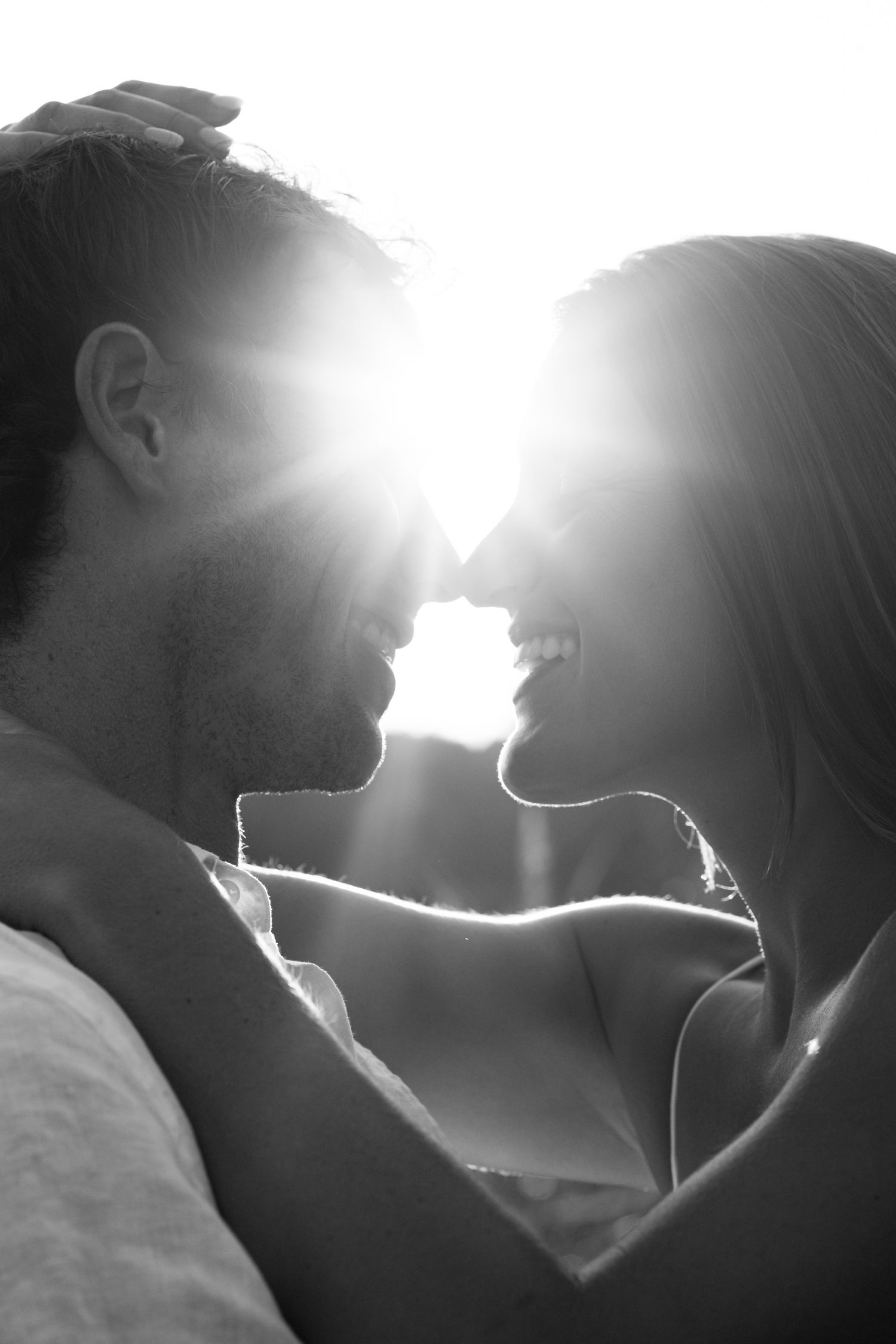 Silhouetted figures share an intimate moment against bright sunlight in a dramatic black and white composition.
