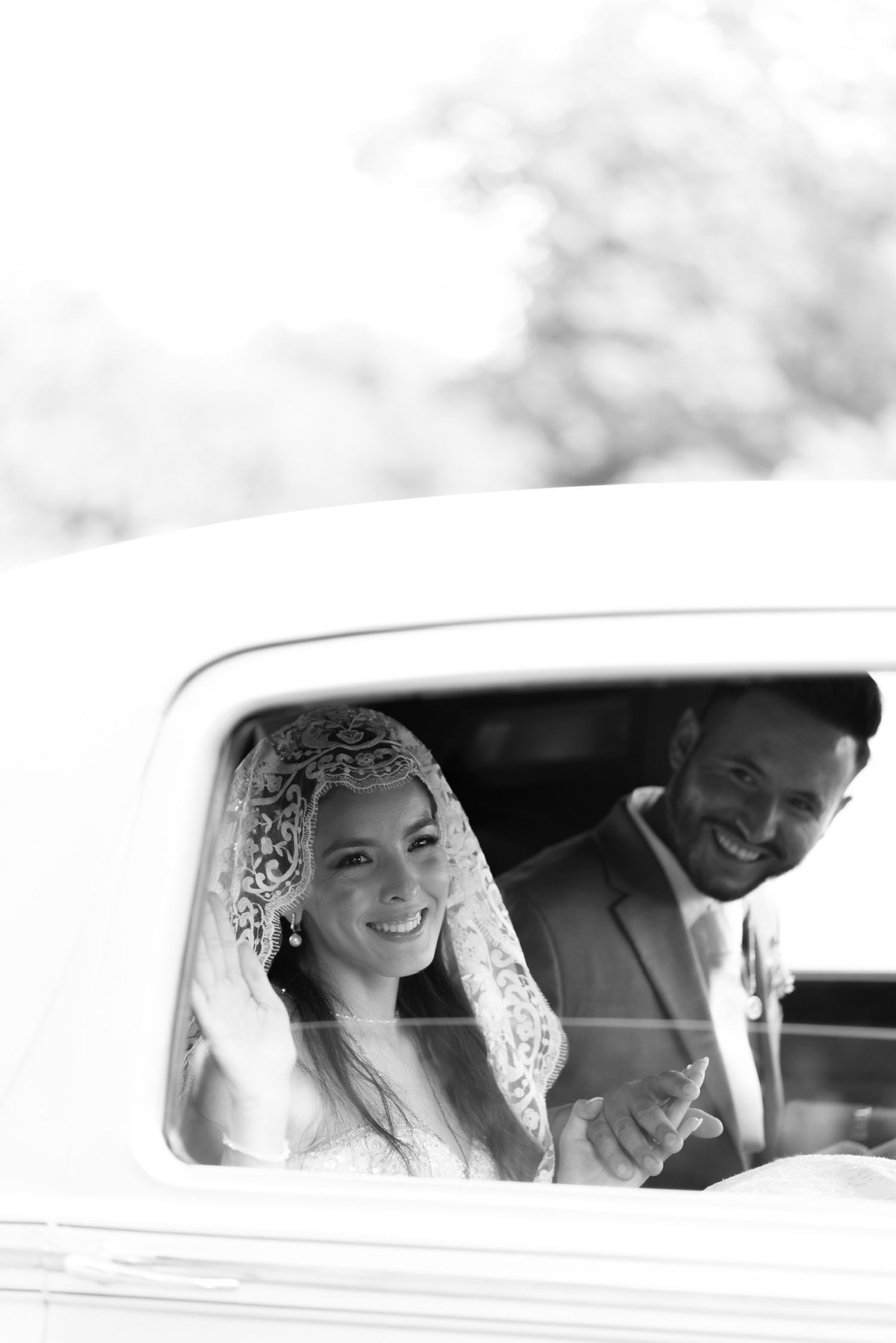Black and white photo of newlyweds smiling inside vintage wedding car.